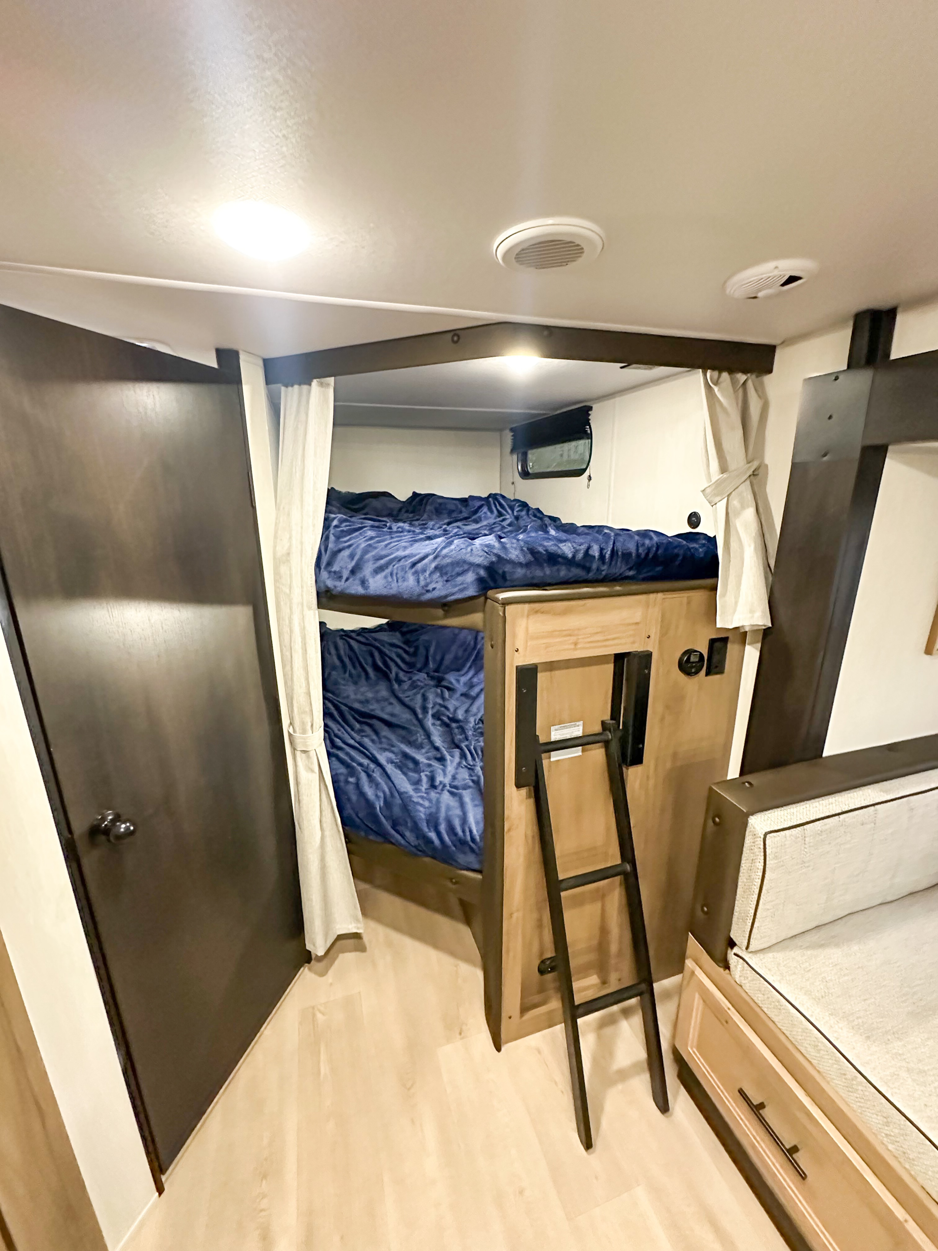 This RV rental features two bunk beds with blue bedding, a ladder, and a light-colored sofa, offering family comfort.. Forest River Grey Wolf 26 DBH 2025