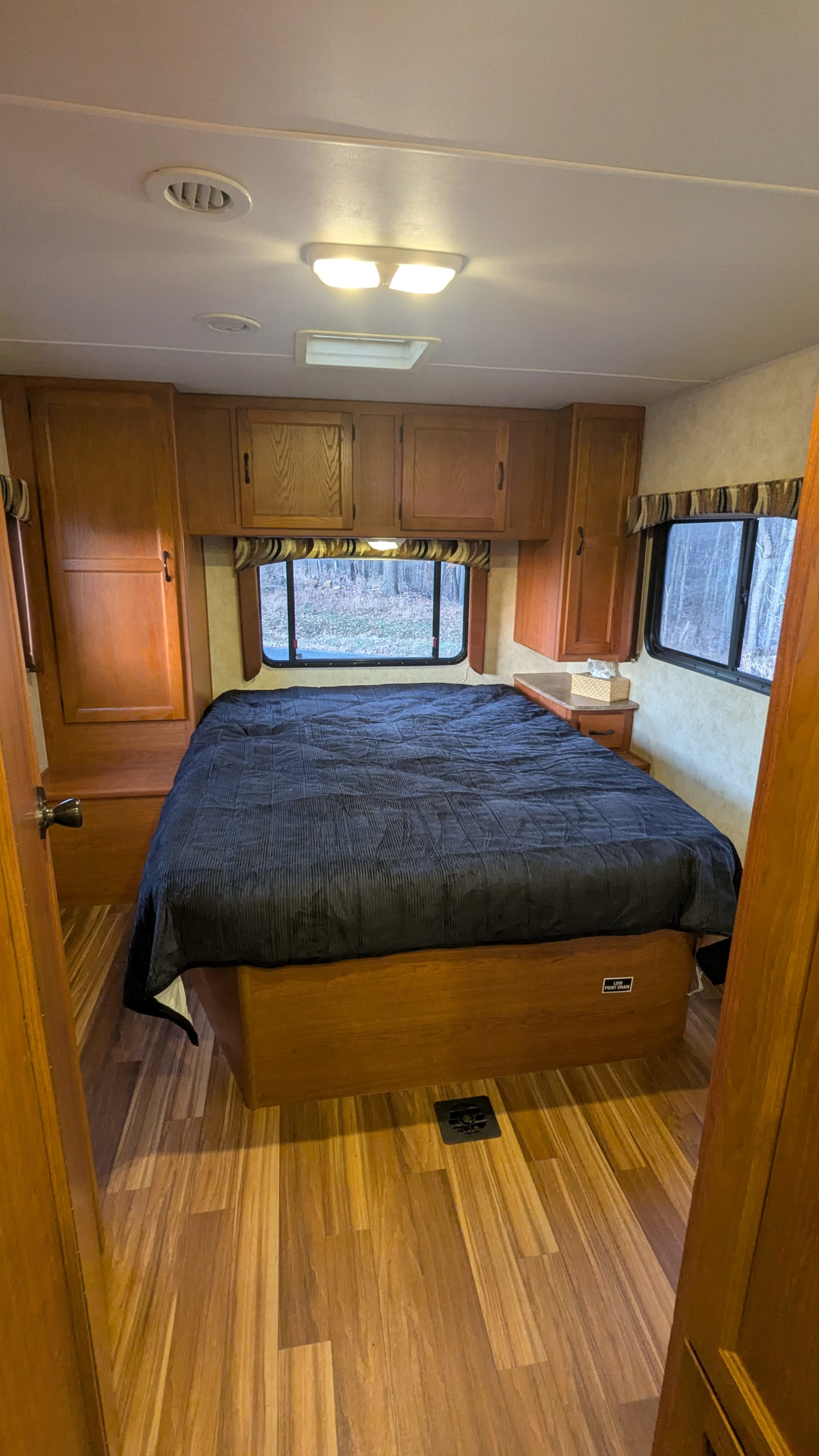 Step into this spacious RV rental bedroom featuring a comfy bed, rich wooden cabinets & floors, and scenic window views.. Forest River Coachmen Freelander 2013