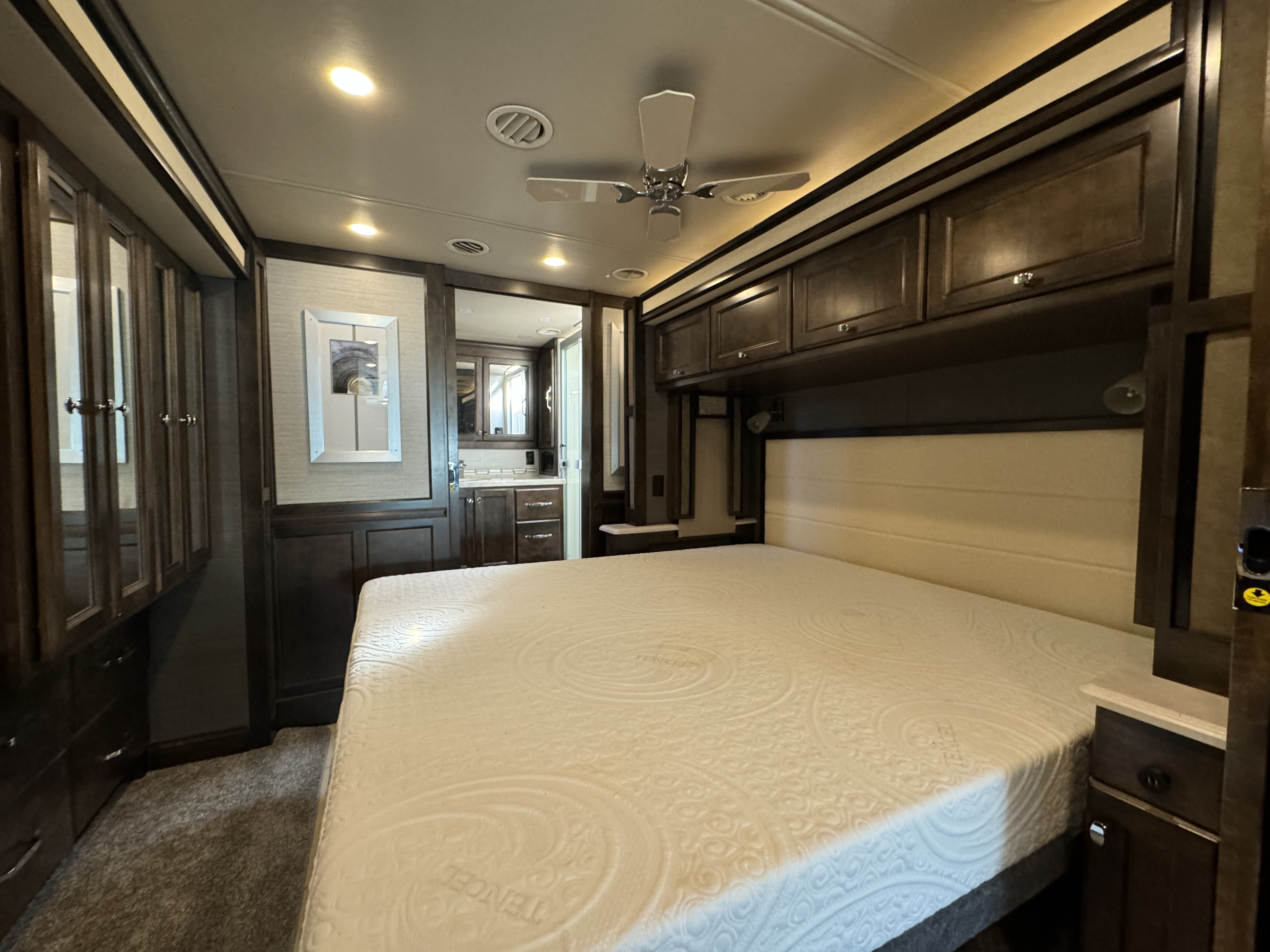 Spacious RV rental bedroom featuring a large bed, overhead cabinets, ceiling fan, and ample storage for comfortable travel.. Tiffin Motorhomes Allegro Red 2020