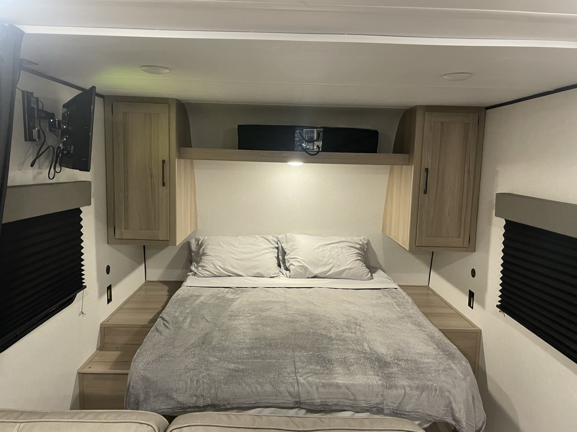Cozy RV rental bedroom featuring a bed with grey bedding, mounted TV, and built-in storage cabinets. Ready for travel.. Keystone Coleman 23B 2025