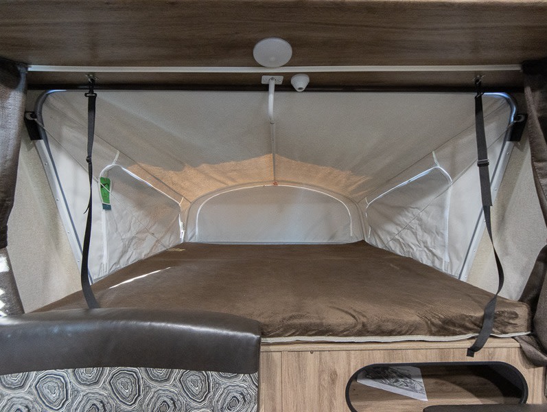 RV rental interior: Pop-up camper bed with brown blanket and fabric walls, showing a cozy expandable sleeping area.. Jayco Jay Feather 2018