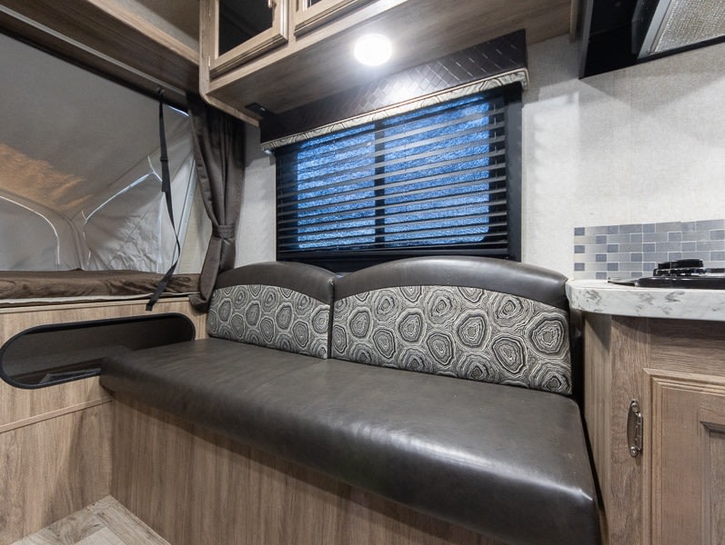 Inside this RV rental: functional dinette with patterned cushions, compact kitchen, and cozy pop-out bed area.. Jayco Jay Feather 2018