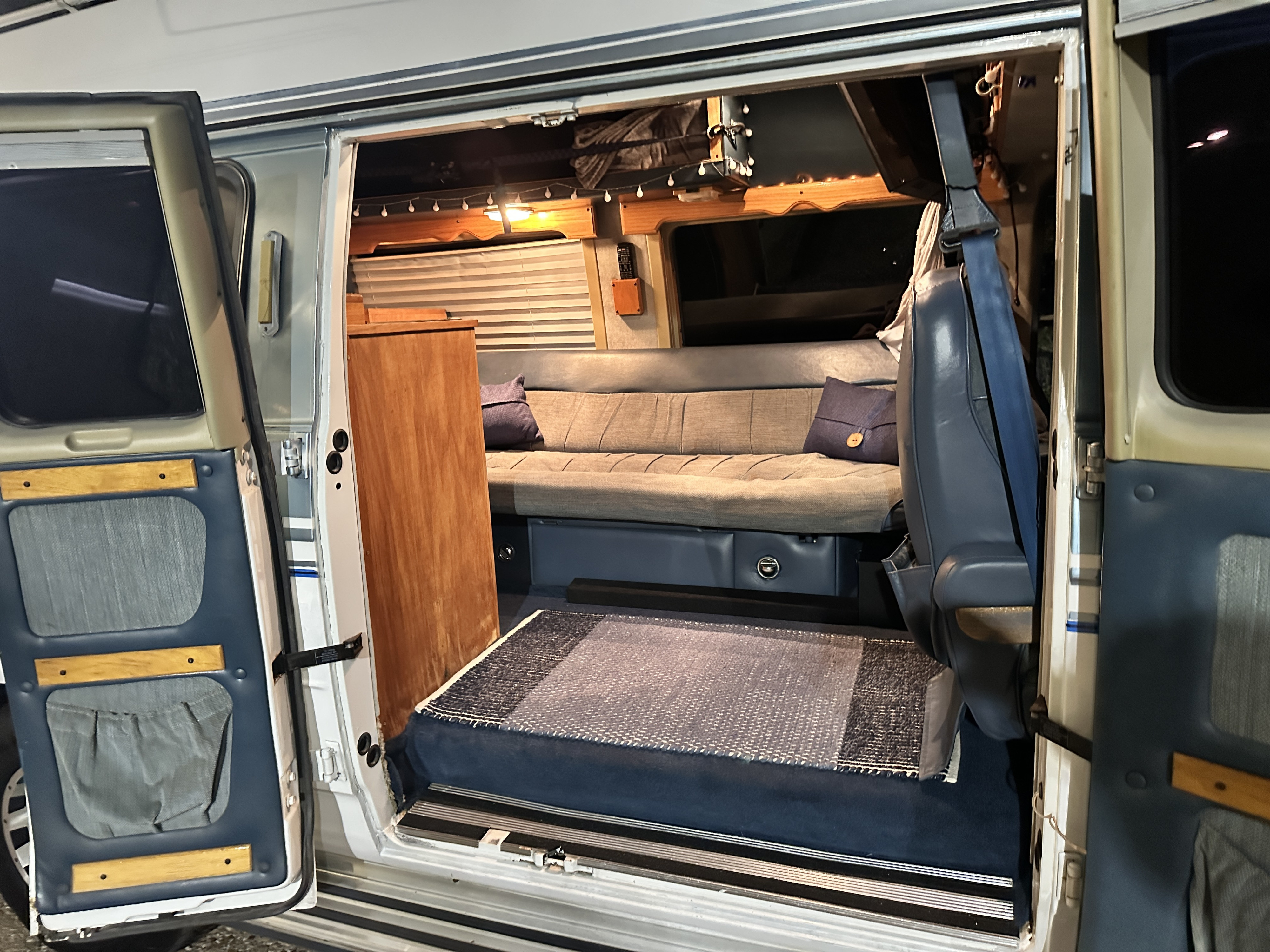 An RV rental's open side door reveals a well-appointed camper van interior with a sofa, wood accents, and lighting.. Chevrolet Rocky Ridge G20 1990
