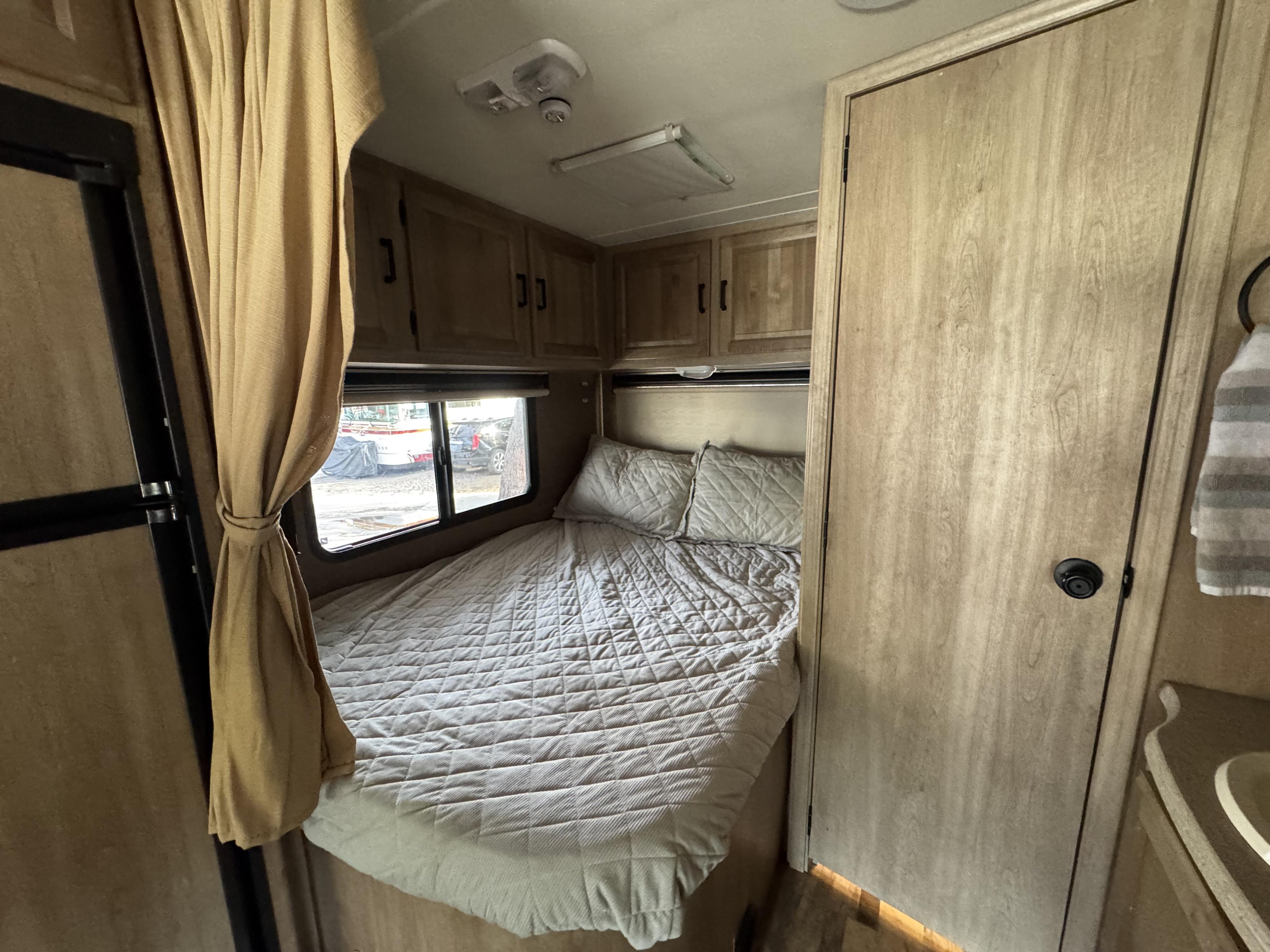 Inside an RV rental: a neat bedroom with a quilted bed, window, wooden cabinets, and door, ready for a cozy journey.. Coach House Mercedes Sprinter Class C 2015