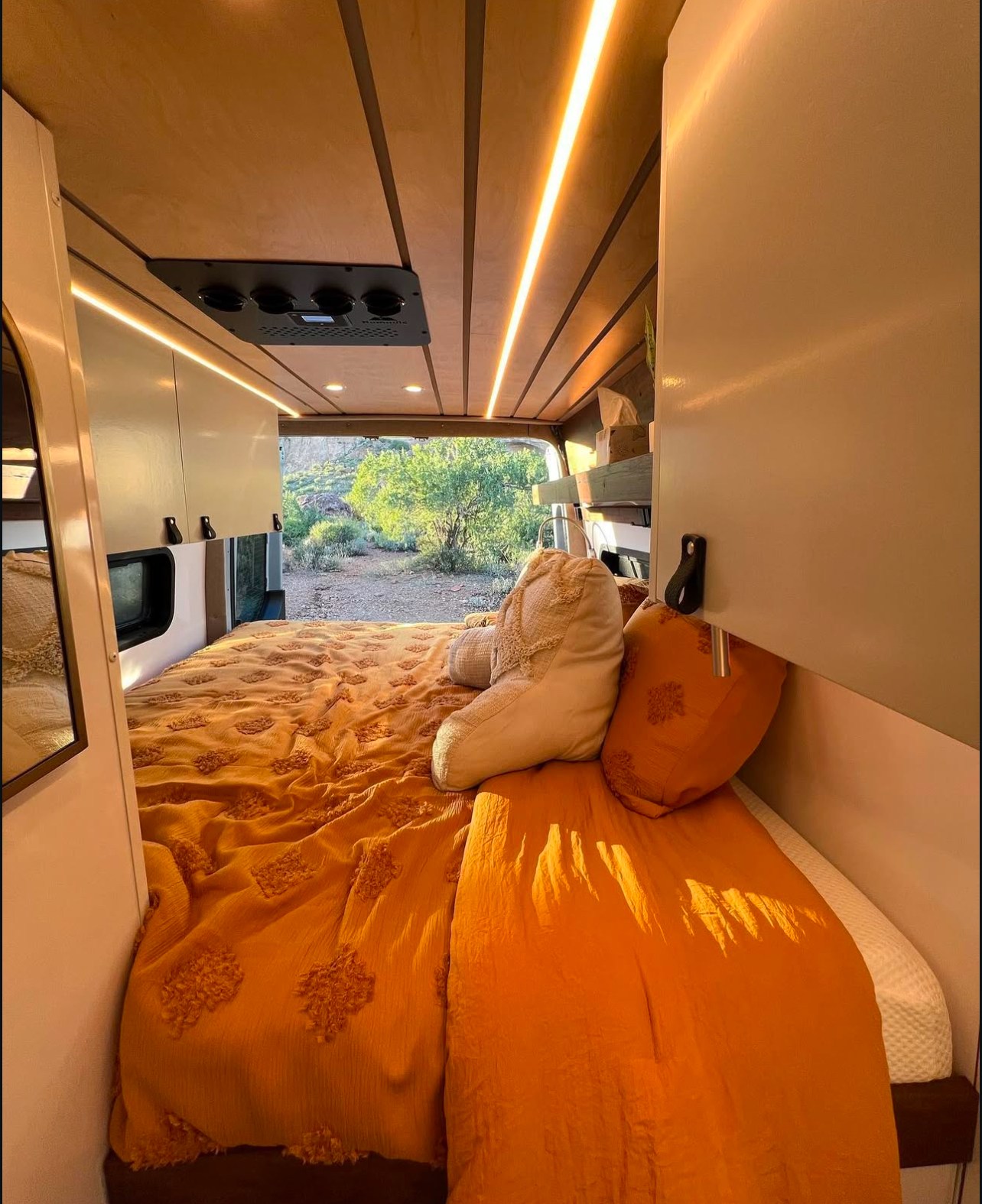 Step into this cozy RV rental's bedroom, featuring a vibrant orange bed, warm ceiling lights, and stunning outdoor views.. Mercedes Sprinter Van 170 4x4 2022