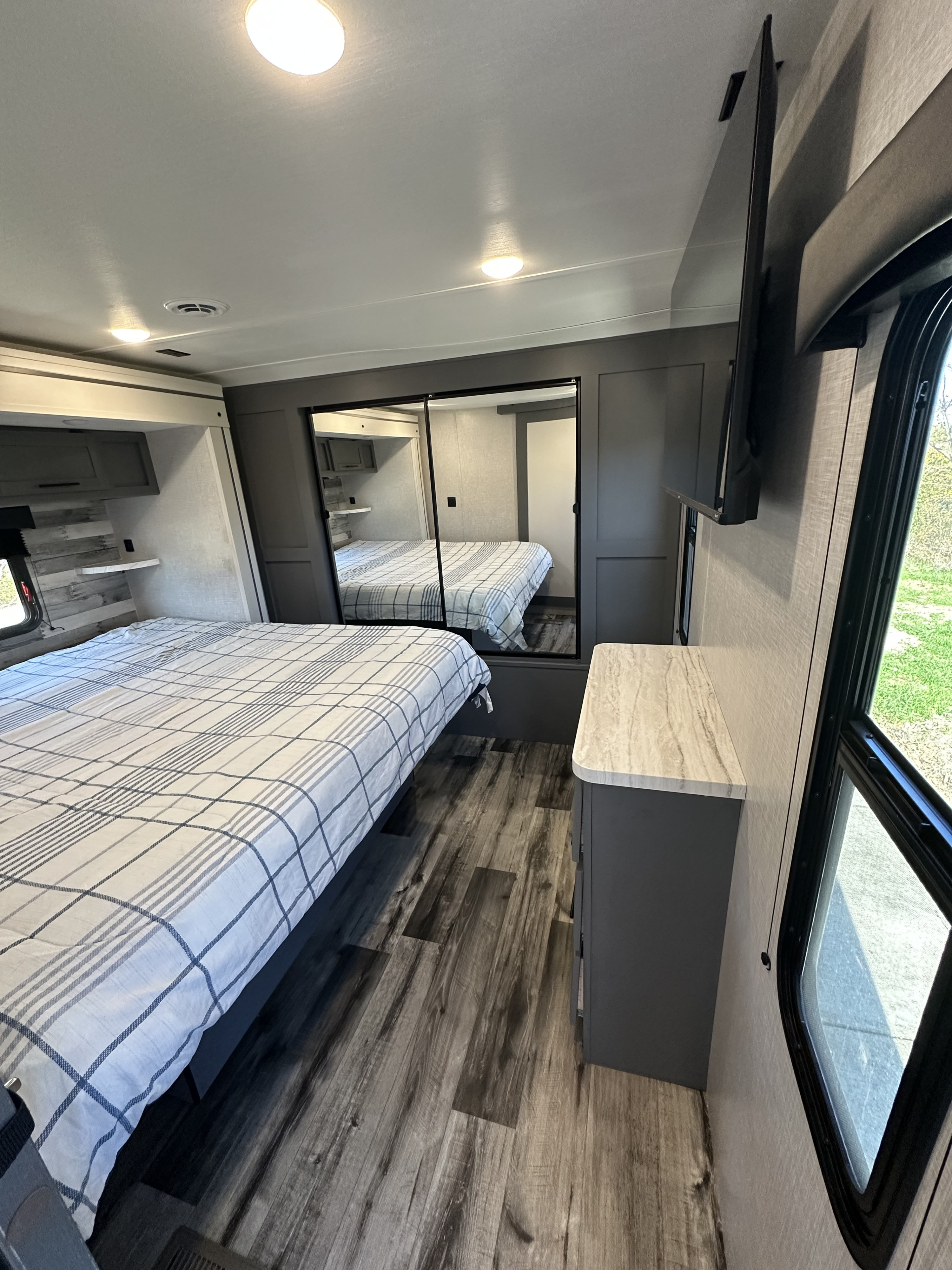Spacious RV rental bedroom featuring a comfy bed, mirrored closet, dresser, and wall-mounted TV. Enjoy the view from large windows.. Crossroads RV Volante 2023