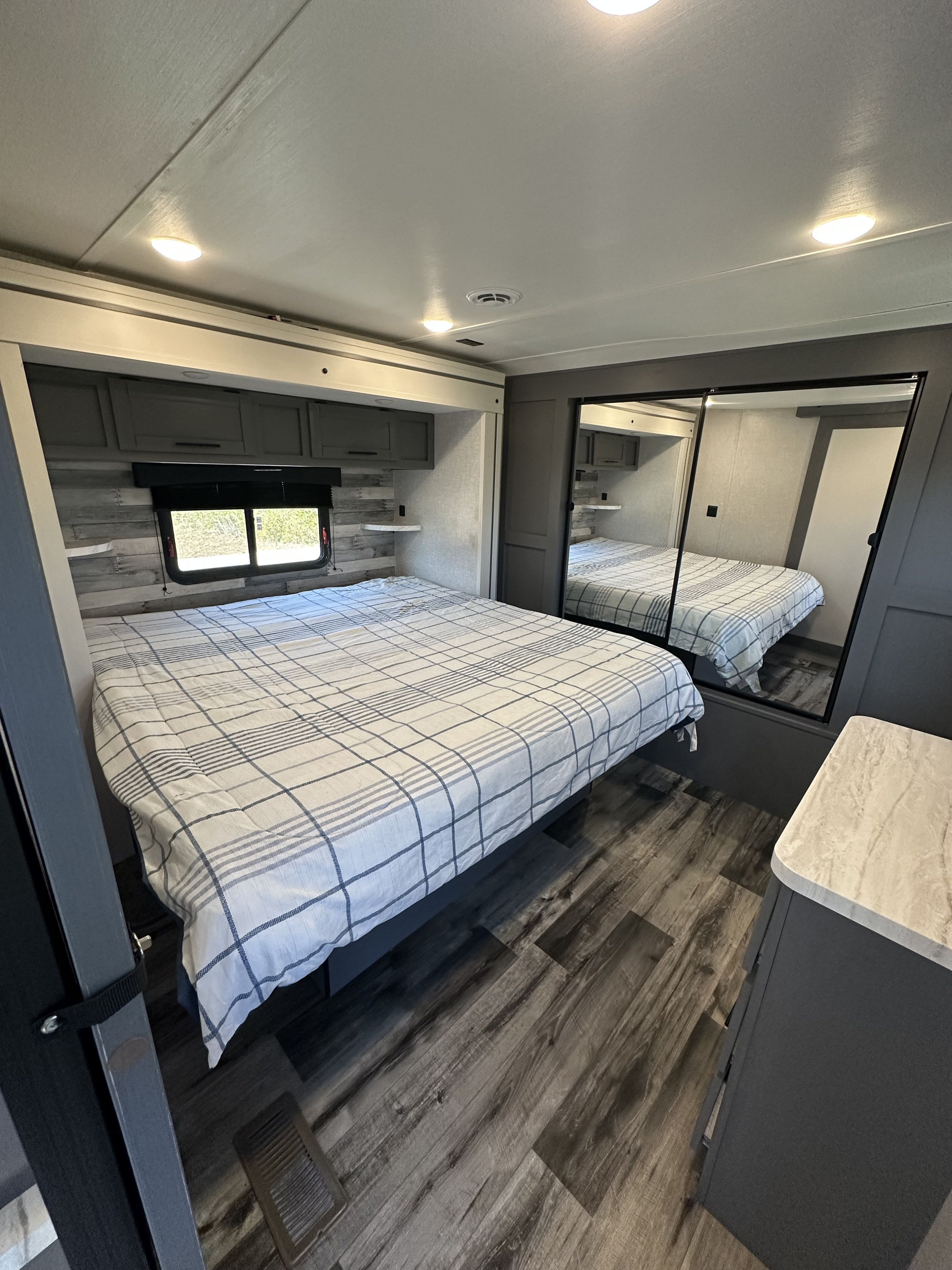 Comfortable RV rental bedroom featuring a plaid bed, overhead cabinets, and a mirrored closet for a spacious feel.. Crossroads RV Volante 2023