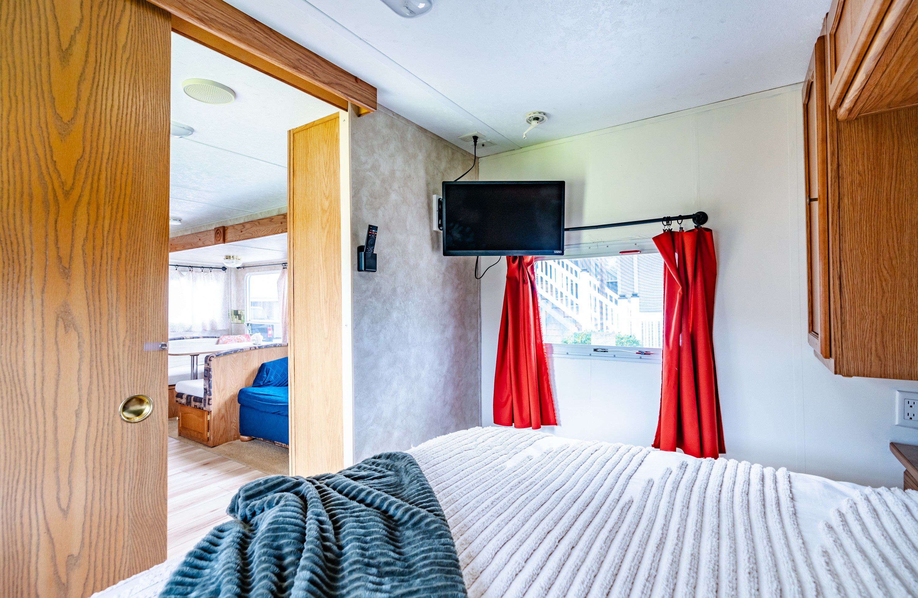 RV rental interior: a cozy bedroom with TV & red curtains, offering a peek into the dining and living area.. Keystone RV Springdale 2006