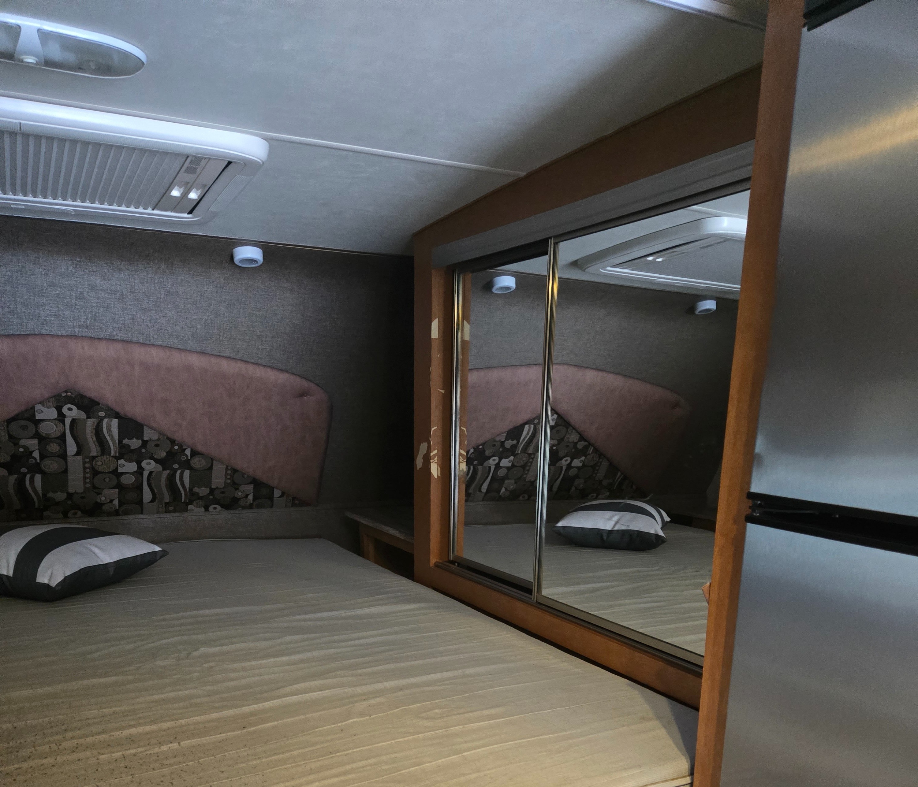 RV rental bedroom: a comfortable bed with a patterned headboard, striped pillow, and mirrored sliding closet door.. Adventurer Adventurer 2018