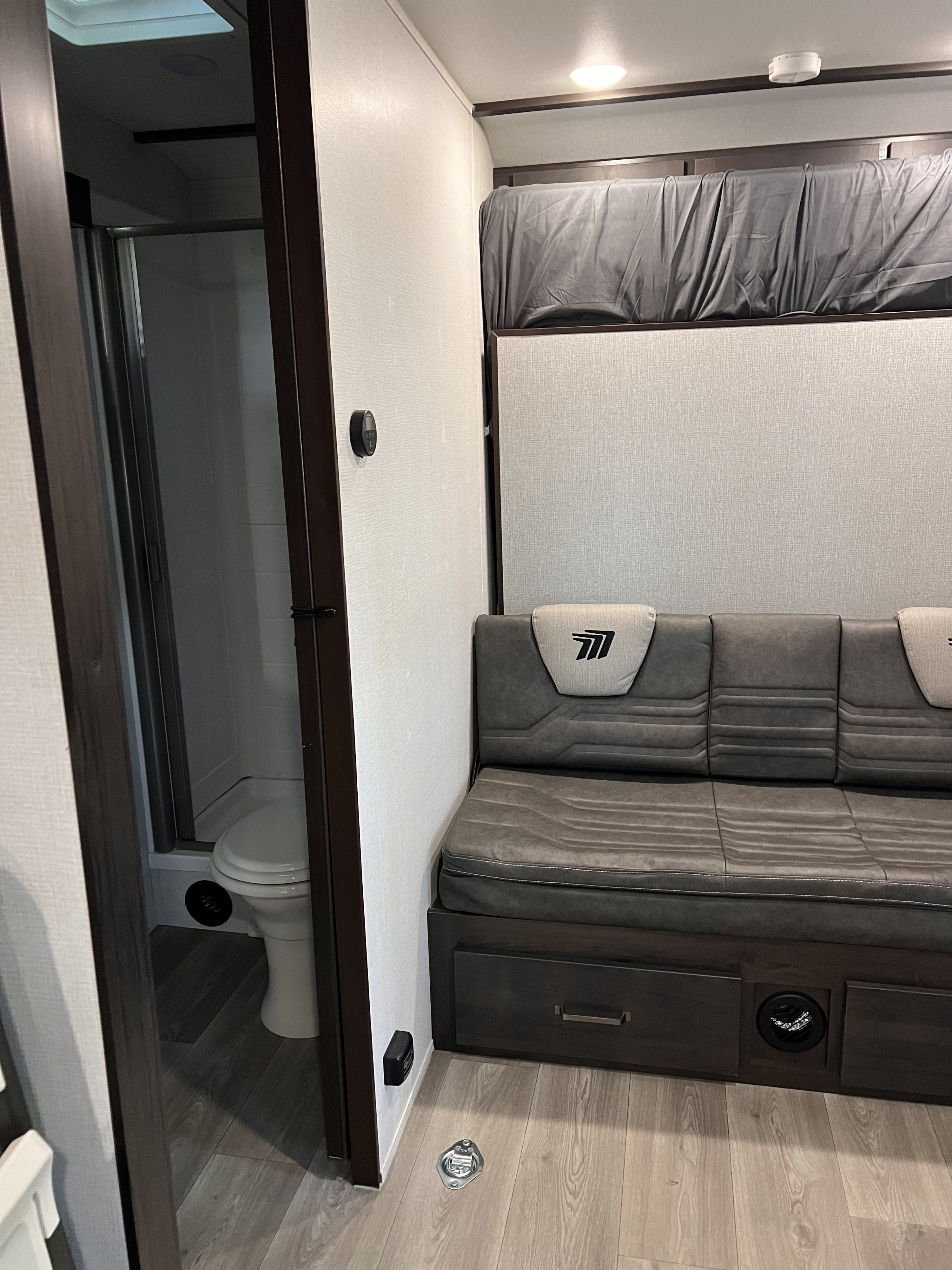 RV rental interior: gray sofa, upper bunk, and a bathroom with toilet & shower on the left.. Grand Design Momentum 2024