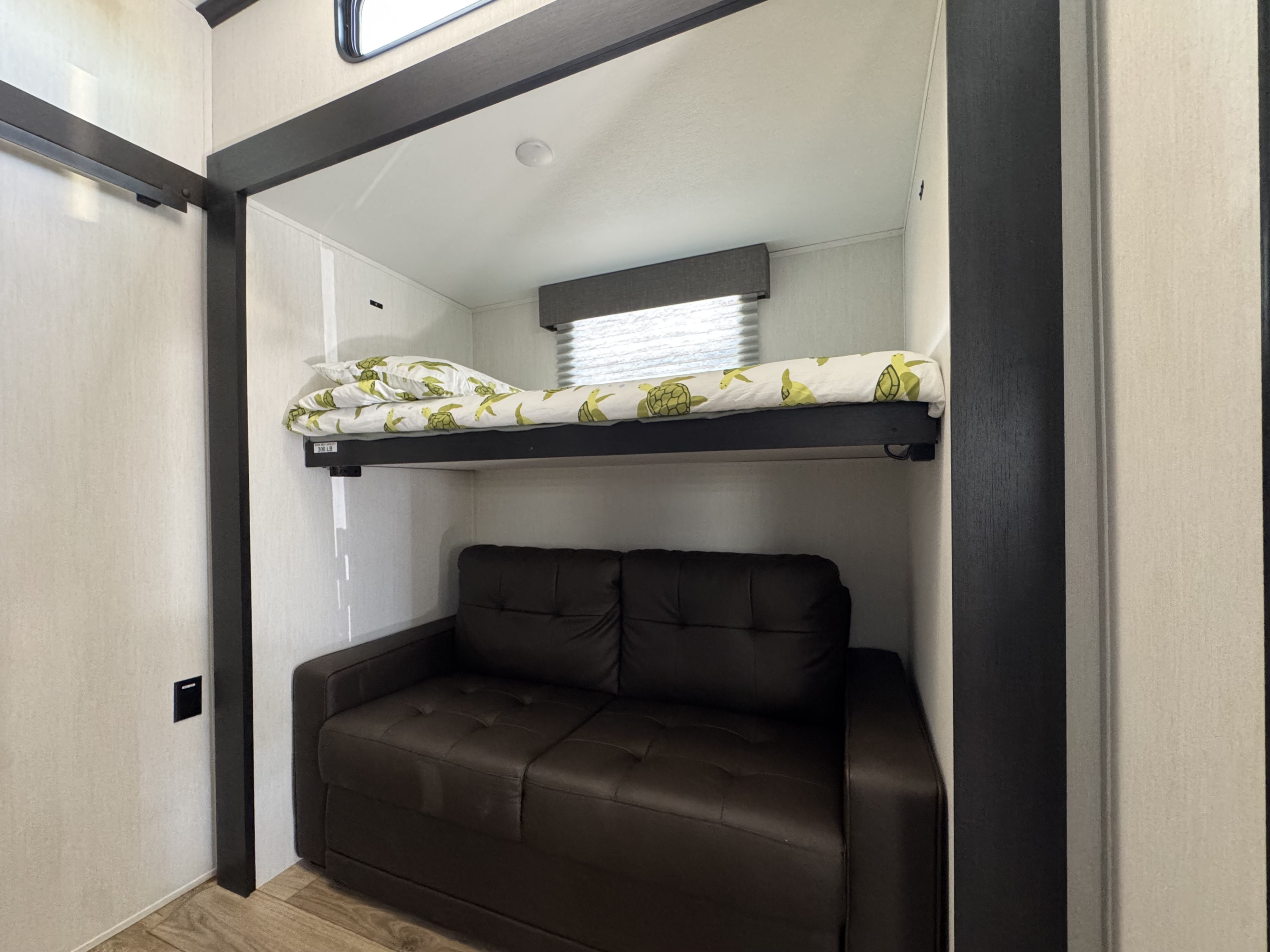 RV rental interior with a practical bunk bed setup: an upper bunk with playful turtle bedding, and a versatile sofa/bed below.. Forest River Sabre 2025