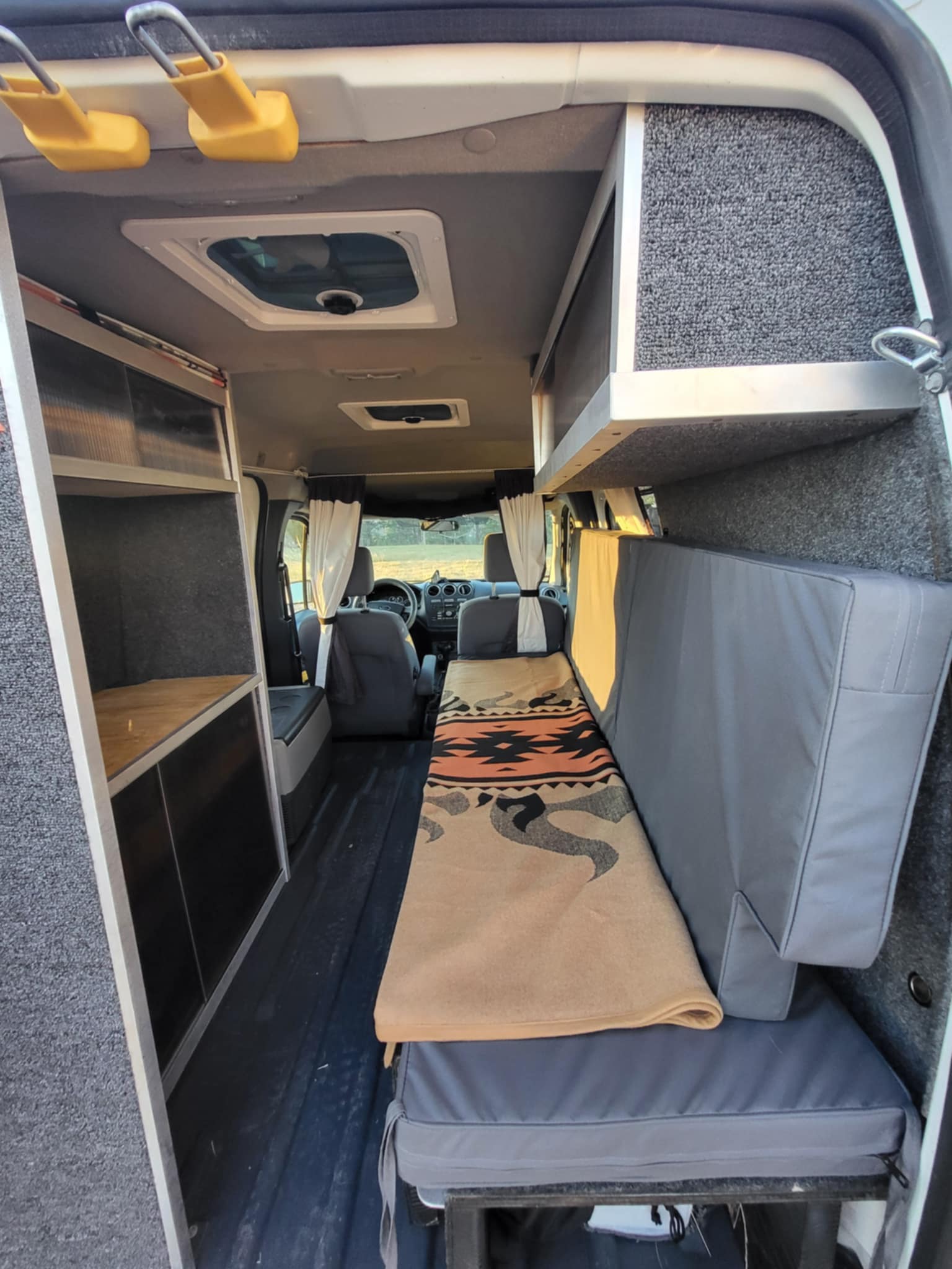 Inside a compact camper van, perfect for an RV rental. Features a sleeping area, modular storage, and roof vents.. Ford Ford Transit 2011