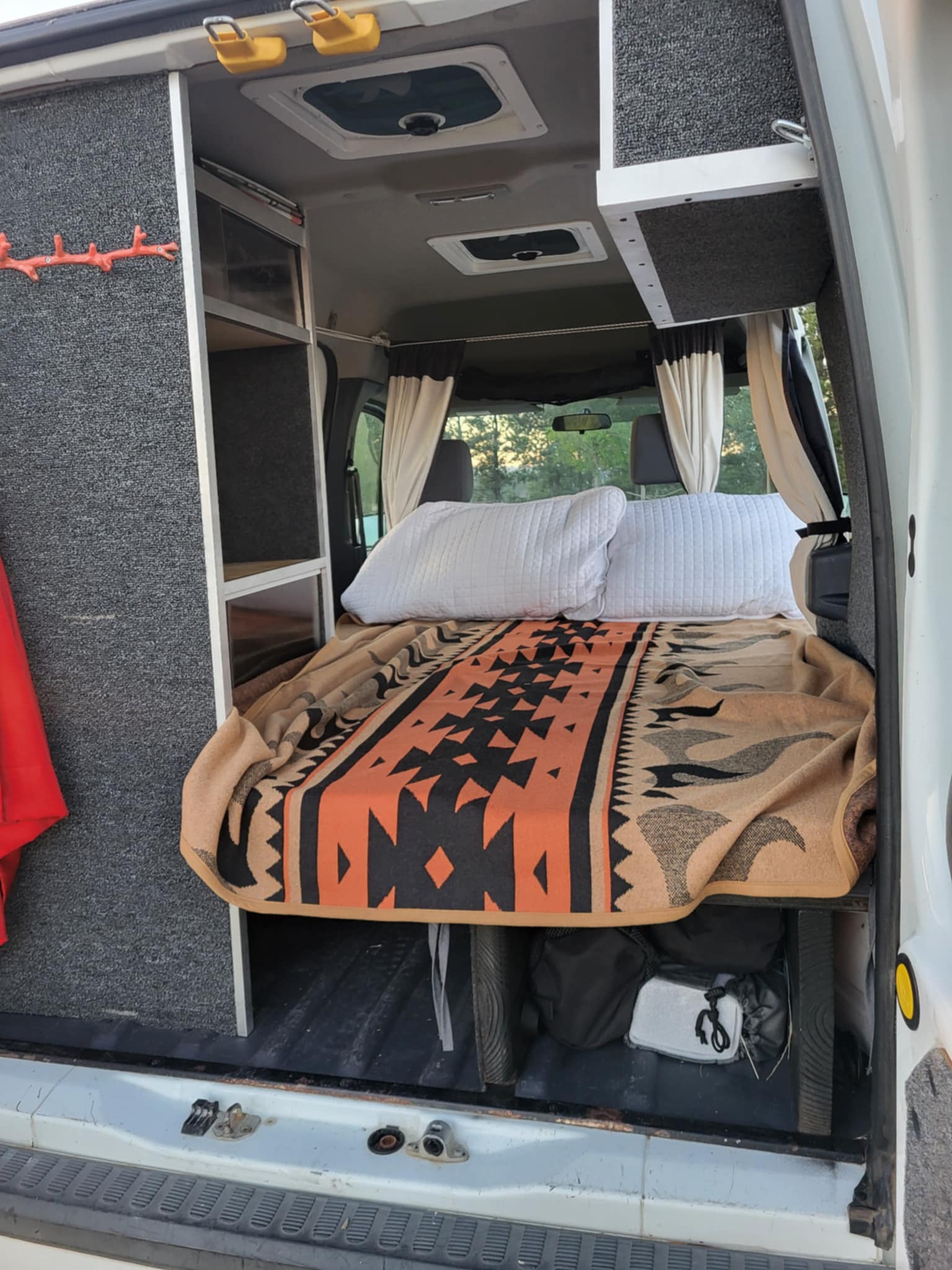 Cozy RV rental camper van interior featuring a comfortable bed with a patterned blanket, built-in storage, and overhead shelves.. Ford Ford Transit 2011
