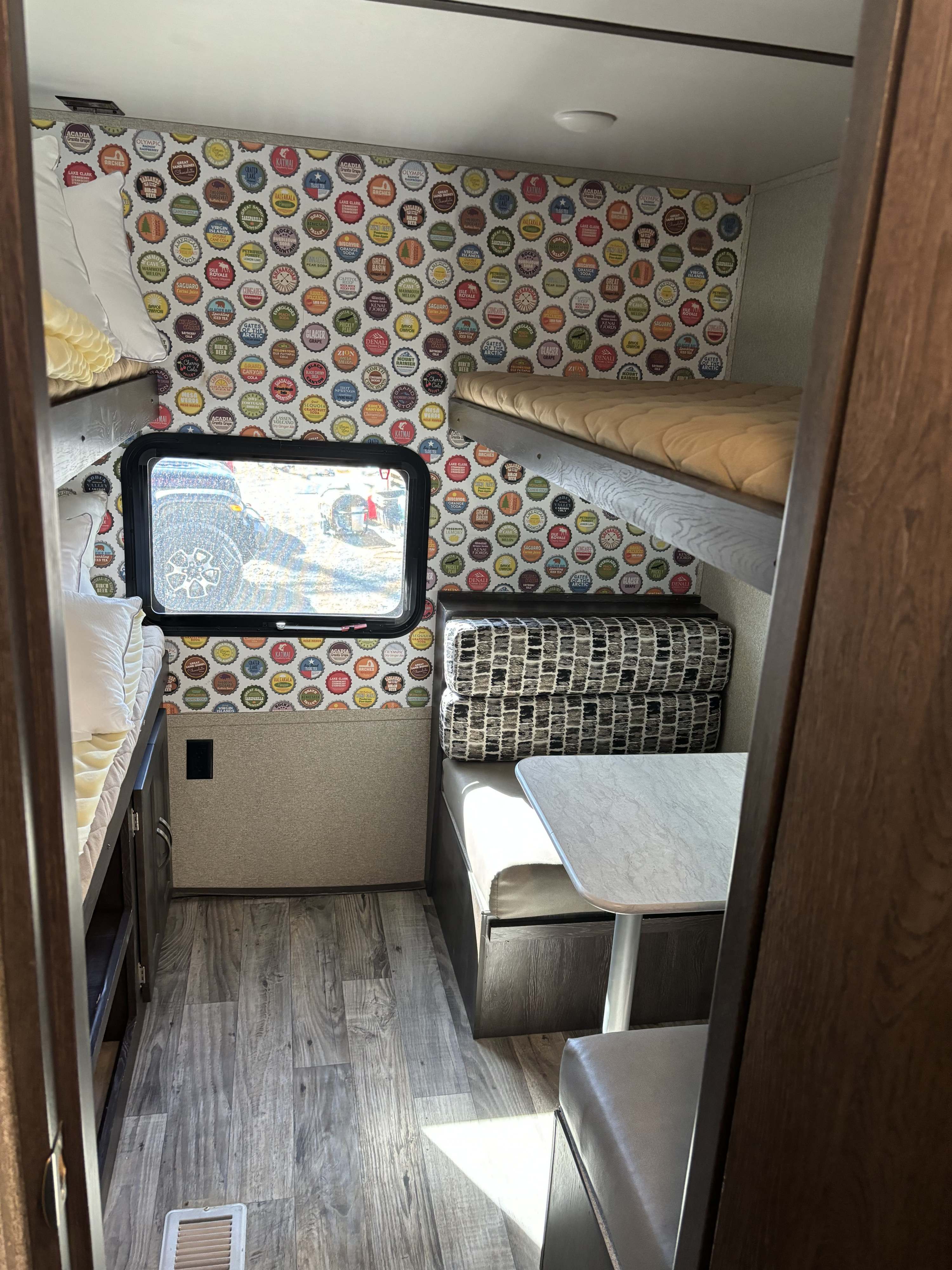Cozy rv rental interior with unique national park bottle cap wallpaper, bunk beds, and a dinette. Perfect for travel adventures!. Keystone RV Outback Ultra-Lite 2018