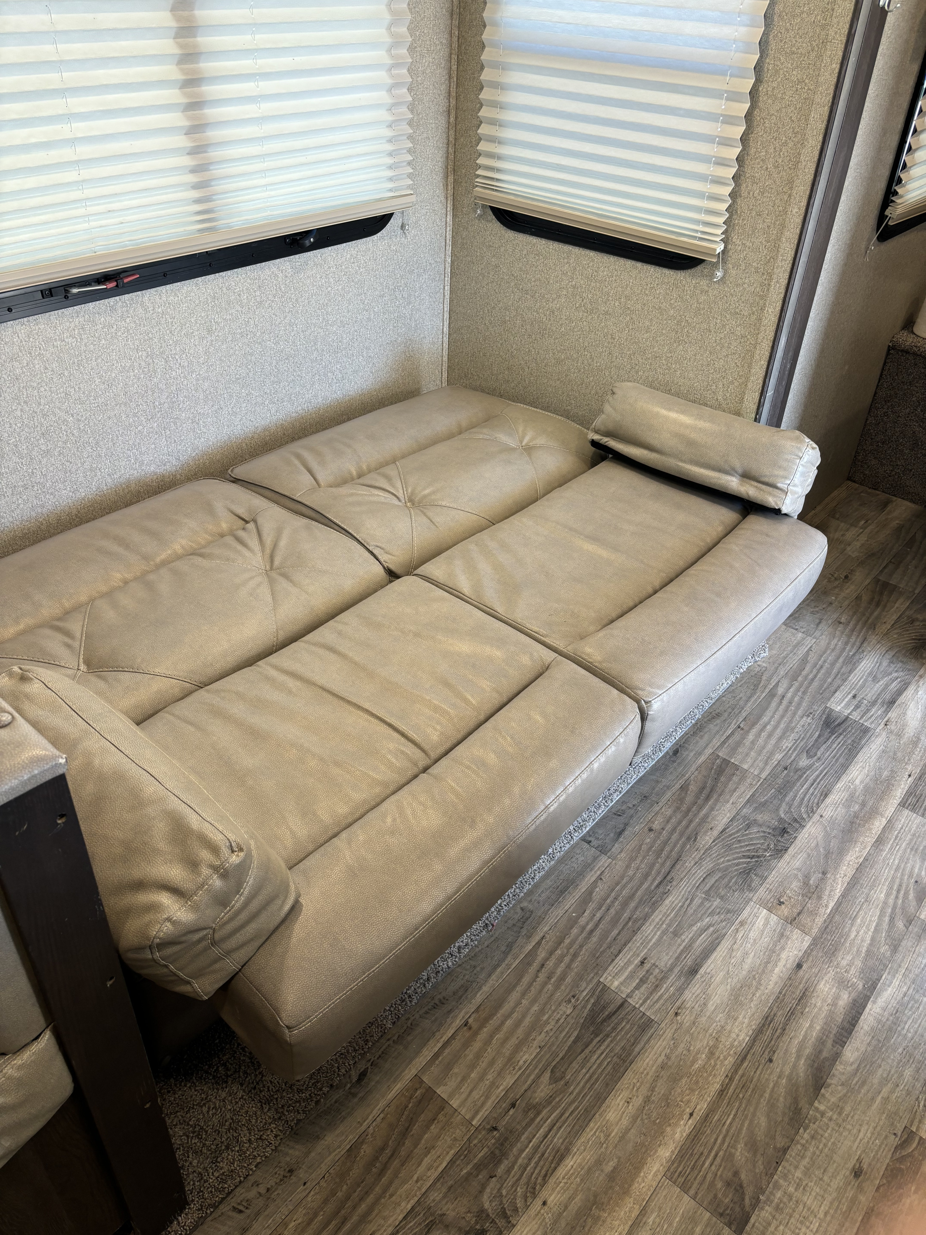Cozy RV rental interior with a beige leatherette convertible sofa, pleated window blinds, and stylish wood-look vinyl flooring.. Keystone RV Outback Ultra-Lite 2018