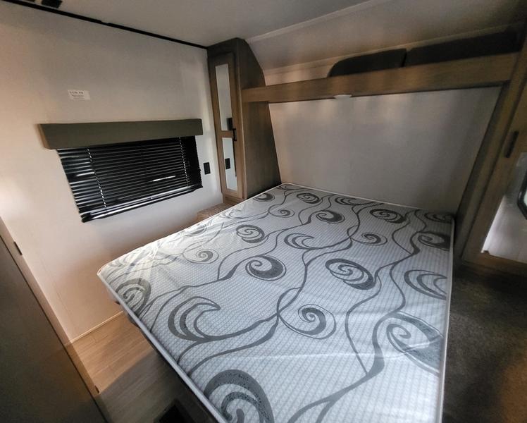 RV rental bedroom with a comfortable bed, window with blinds, and built-in storage in a travel trailer.. Keystone Hideout 2021
