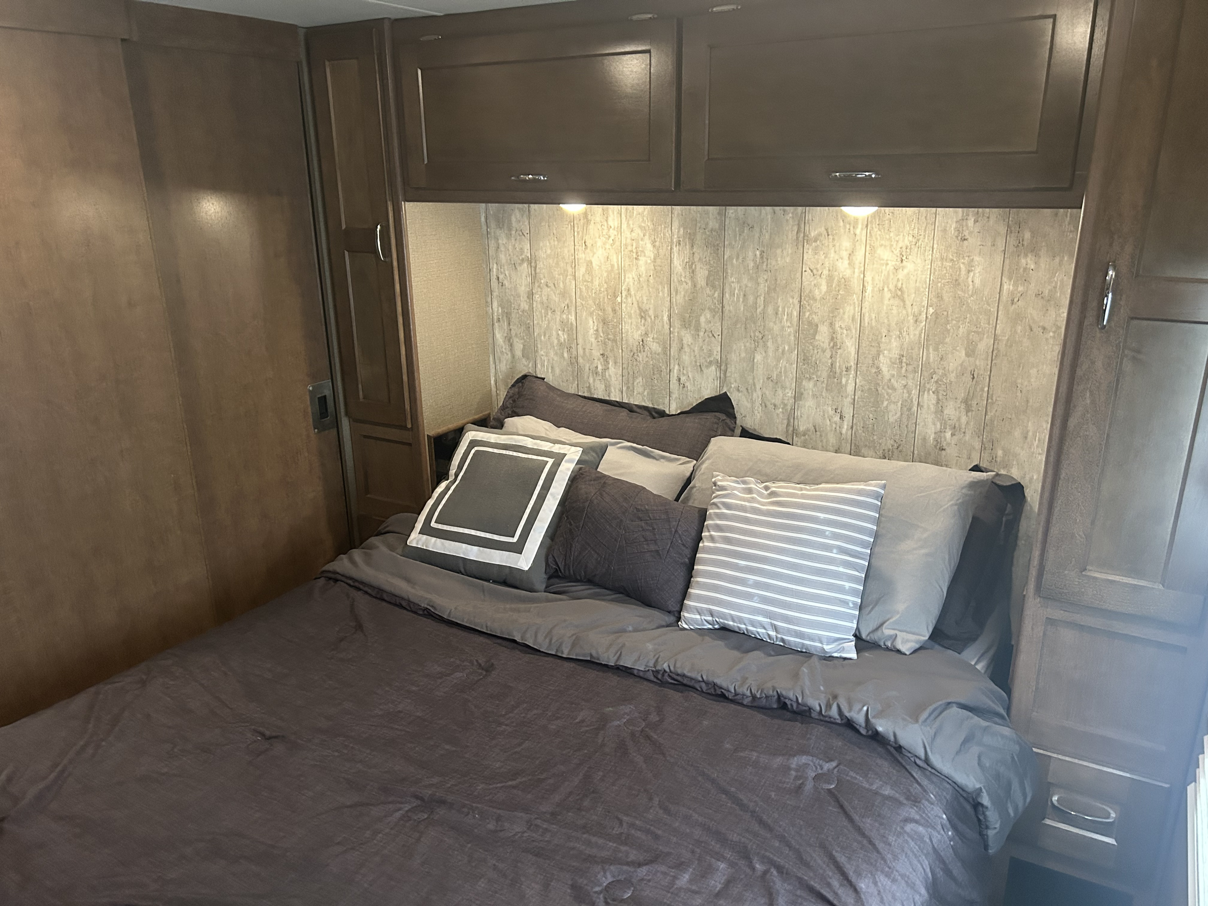 Spacious RV rental bedroom featuring a comfy bed with ample pillows, dark overhead cabinets, and warm under-cabinet lighting.. Winnebago Intent 2018