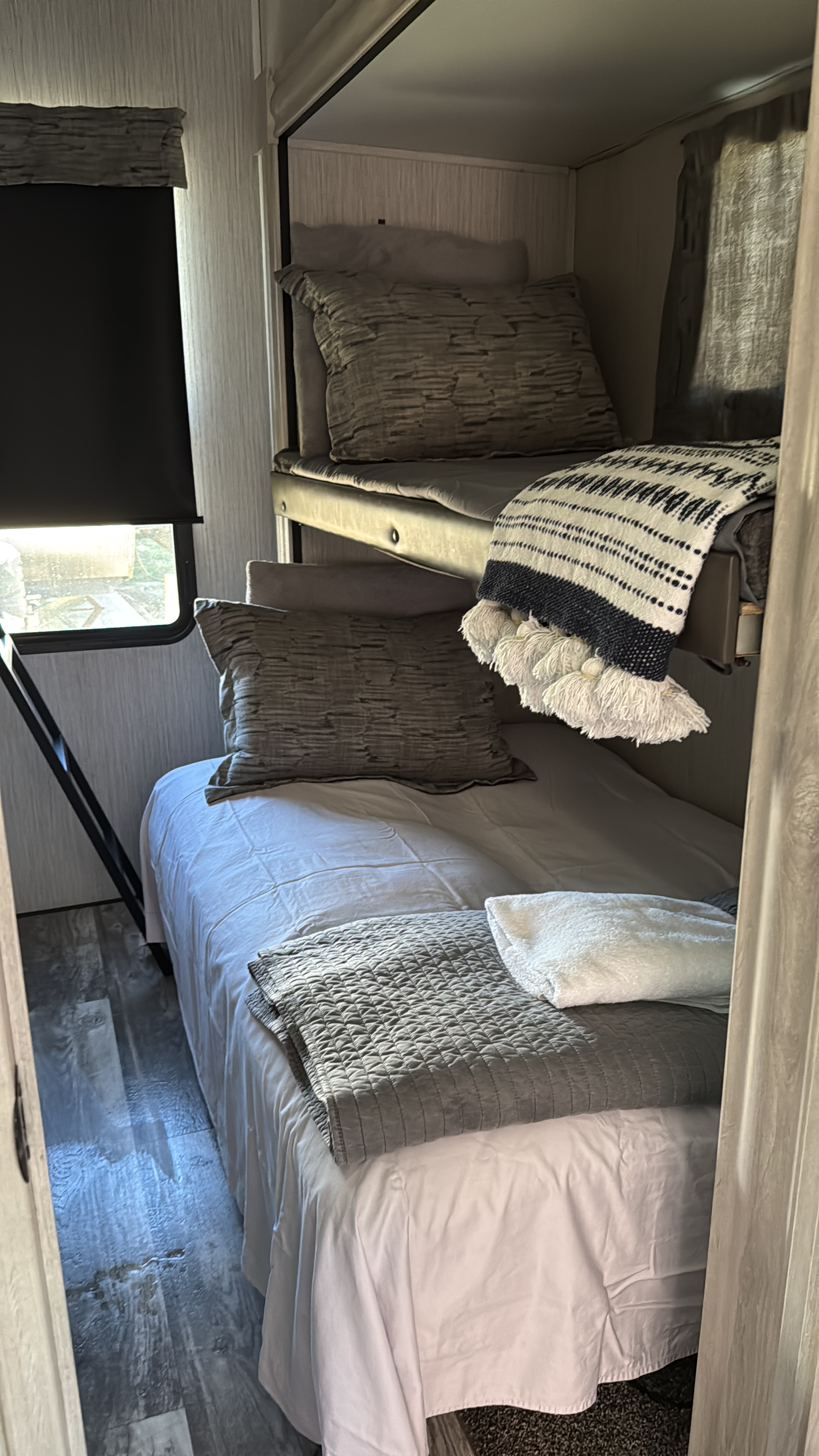Cozy bunk bed setup in an RV rental, featuring comfortable bedding, a window with a blind, and wood-look flooring.. Dutchmen Kodiak Ultra Lite 2022