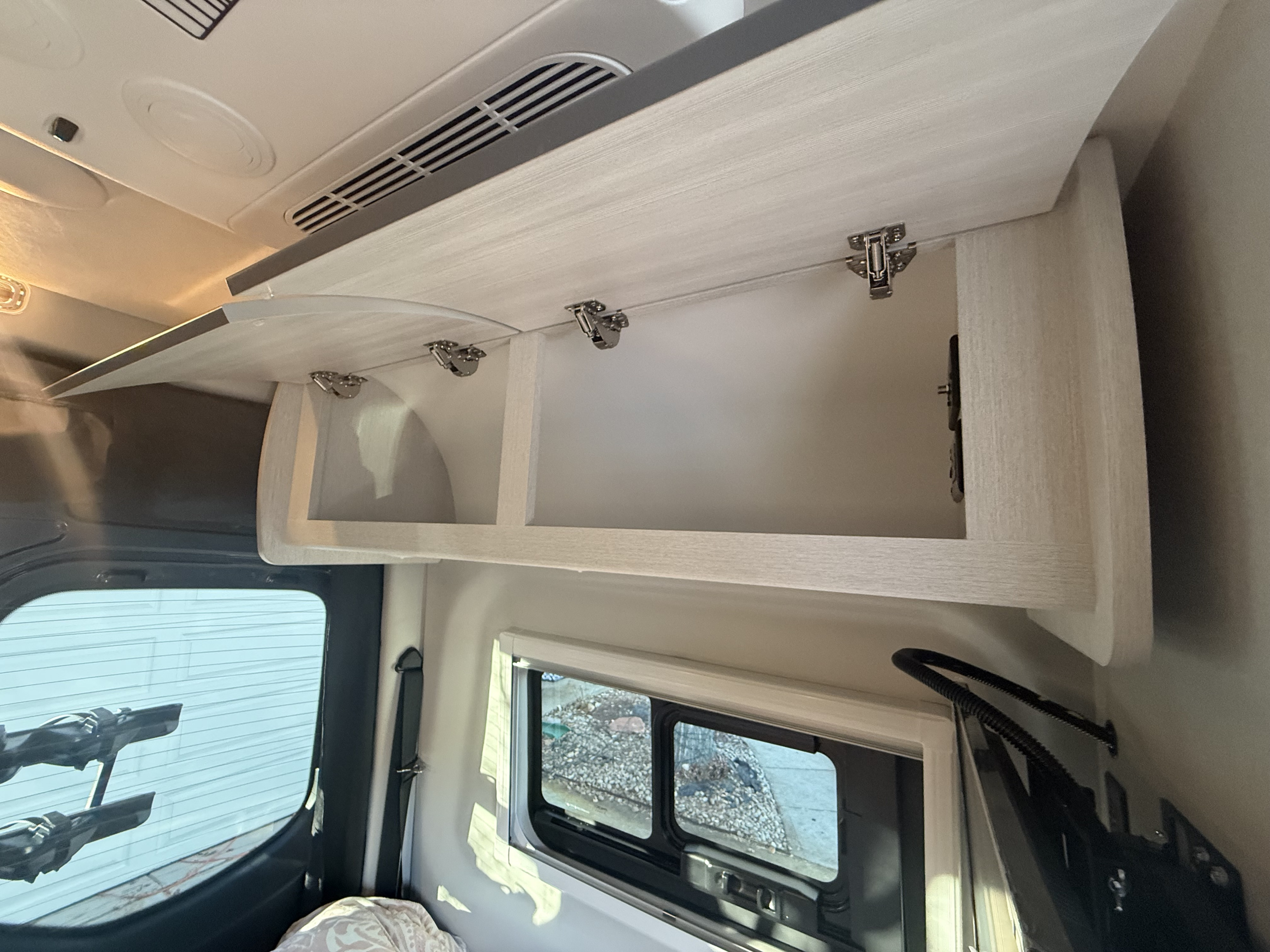 Inside an RV rental: Open overhead cabinets with light wood grain, ceiling vents, and side windows for storage and comfort.. Mercedes-Benz Thor Sanctuary 19p 2025