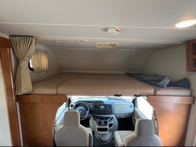 RV rental interior: A spacious cab-over bunk bed with curtains above the driver's area, showing the dashboard and seats.. Winnebago Minnie Winnie 2017