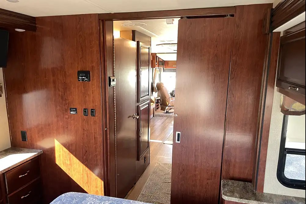 Cozy RV rental interior: wood-paneled bedroom area, hallway, and open sliding doors leading to the front living space.. Flair-Fleetwood LXE 2018