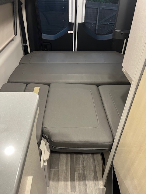 Inside an RV rental: a flexible rear living area with grey modular cushions converts to a bed. Ideal for travel.. Thor Tranquility 2023