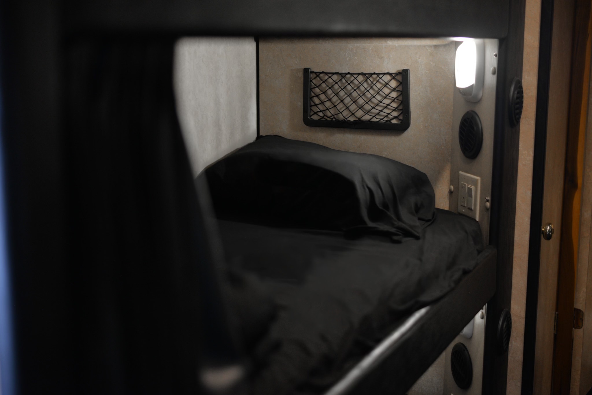 Experience comfort in your RV rental with this compact sleeping nook. Features include a black bed, reading light, vents, and storage net.. Freightliner M2 106 Medium Duty 2018