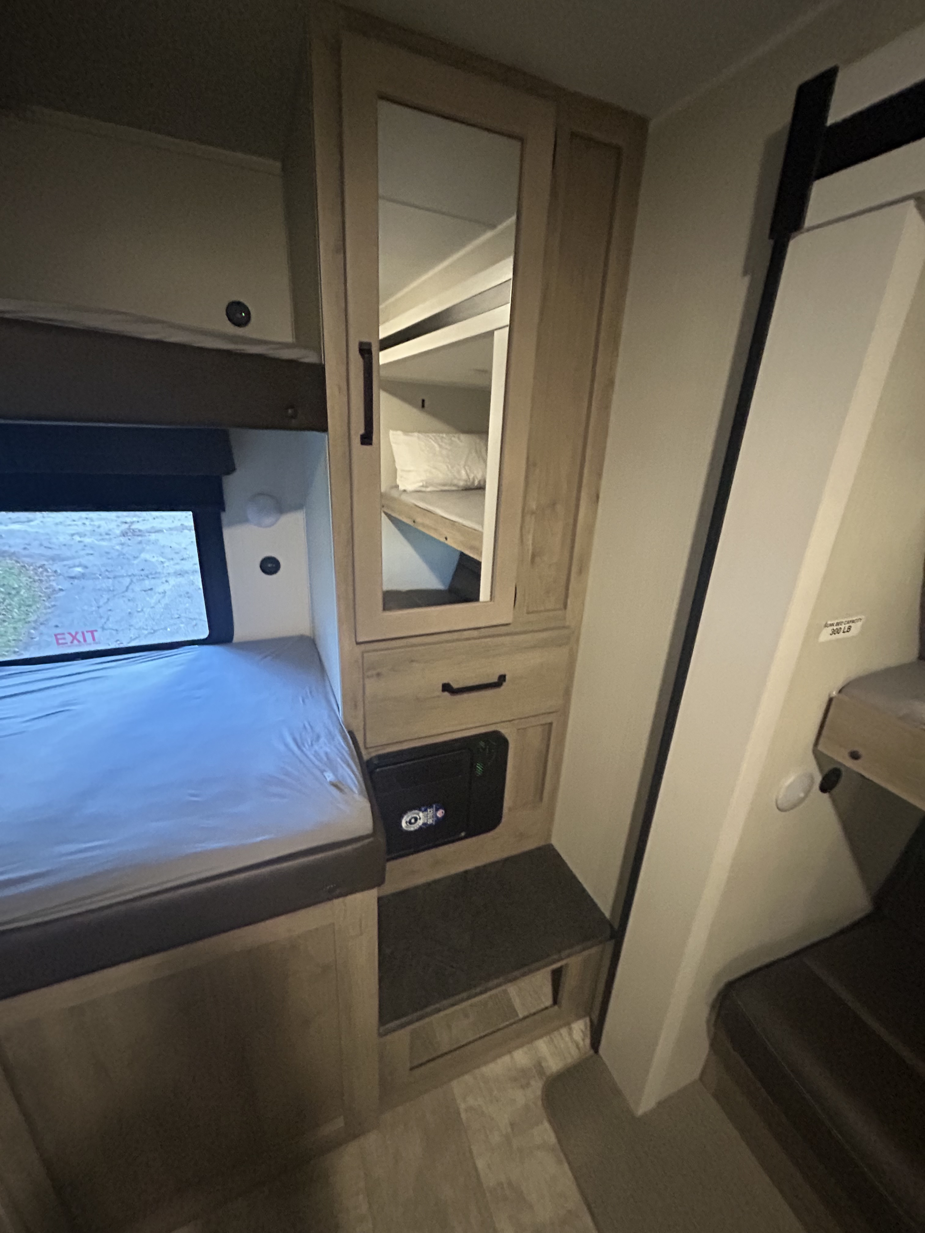 RV rental interior: lower bunk by window (EXIT), mirrored cabinet, and electrical panel. Ladder leads to upper bunk.. Forest River Palomino Puma 2024