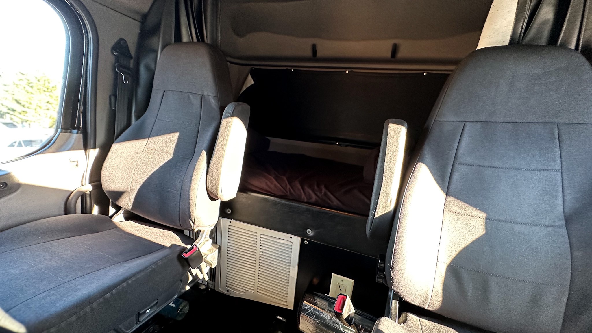 Interior of a truck sleeper cabin shows two seats, a bed, and an outlet. A comfortable mobile living space, like an RV rental.. Freightliner M2 106 Medium Duty 2018
