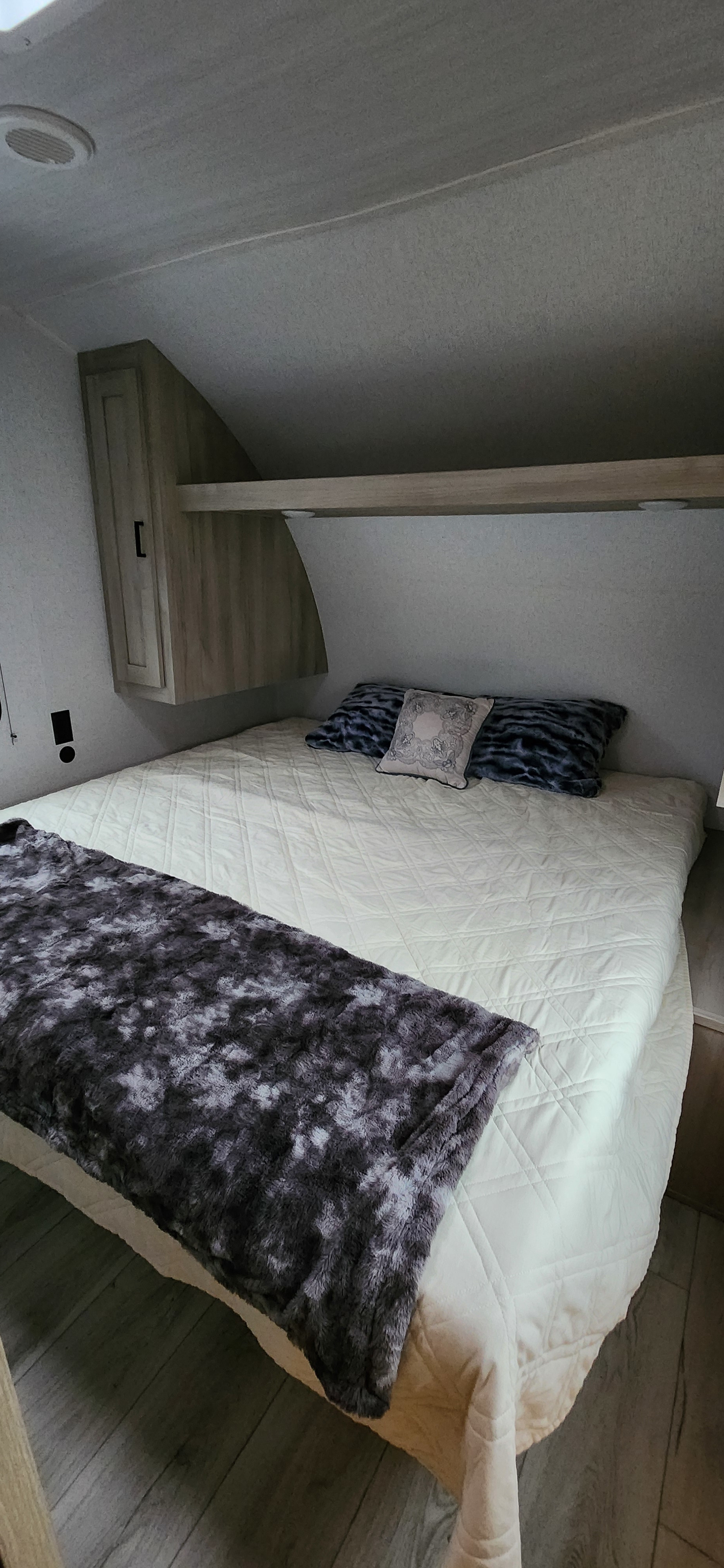 Bedroom in an rv rental: a bed with a quilted comforter, soft furry throw, and built-in overhead storage.. East to West Silver Lake 2024