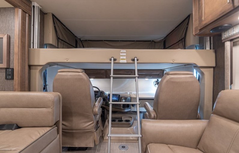 Looking forward in an RV rental, showing the spacious interior with a bunk bed, ladder, and front cockpit seating.. Thor Challenger 2021