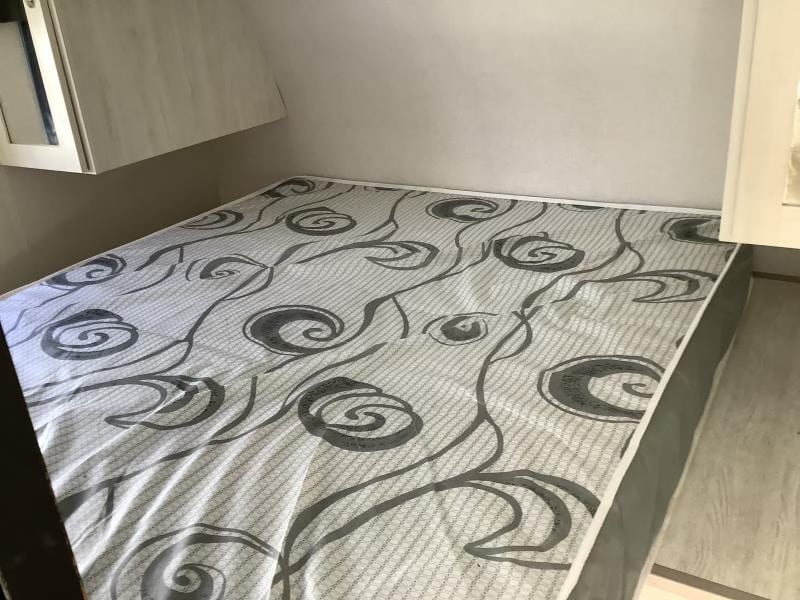 RV rental bed with patterned mattress & overhead cabinets. A cozy, compact sleeping area.. Forest River Tracer LE 2022