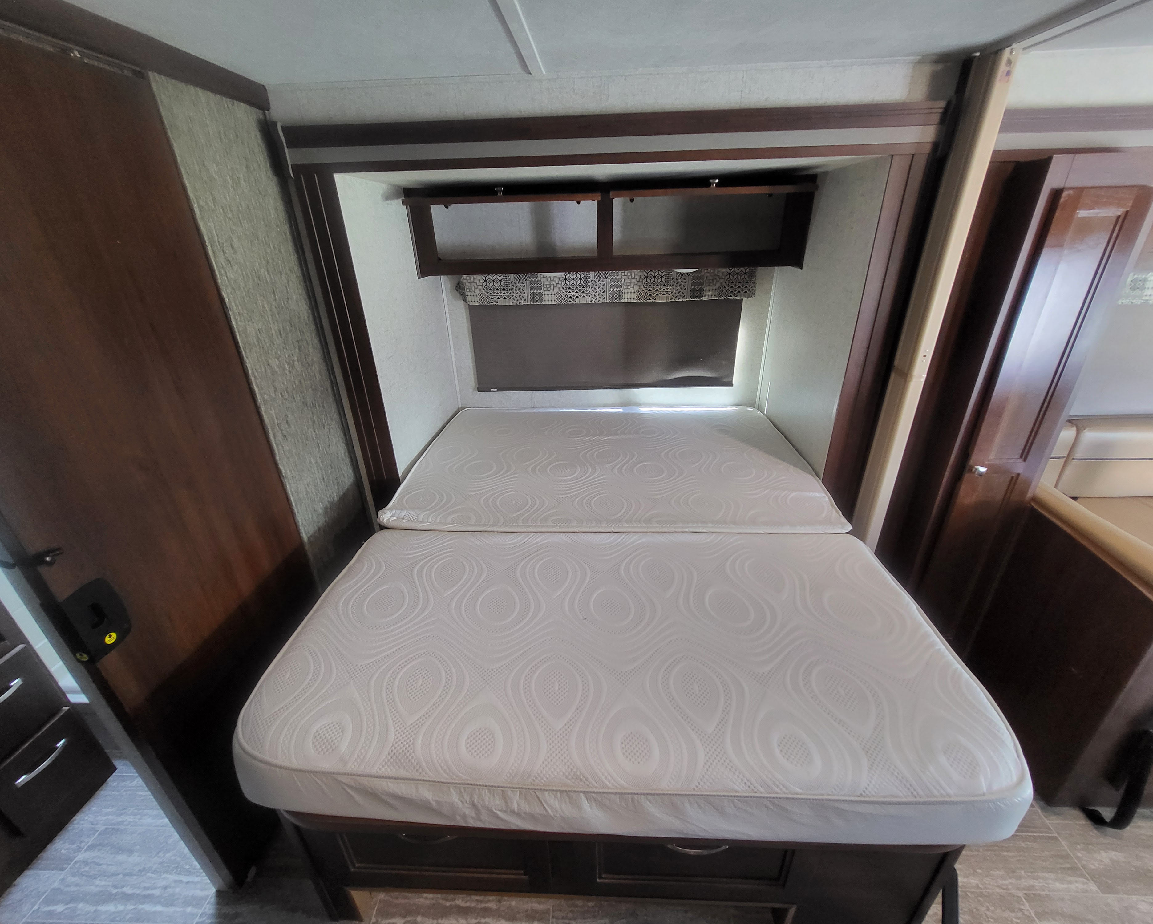 RV rental bedroom with a white, two-piece mattress bed, dark wood cabinetry, overhead storage, and window shade.. Forester Forester Motorhome 2019