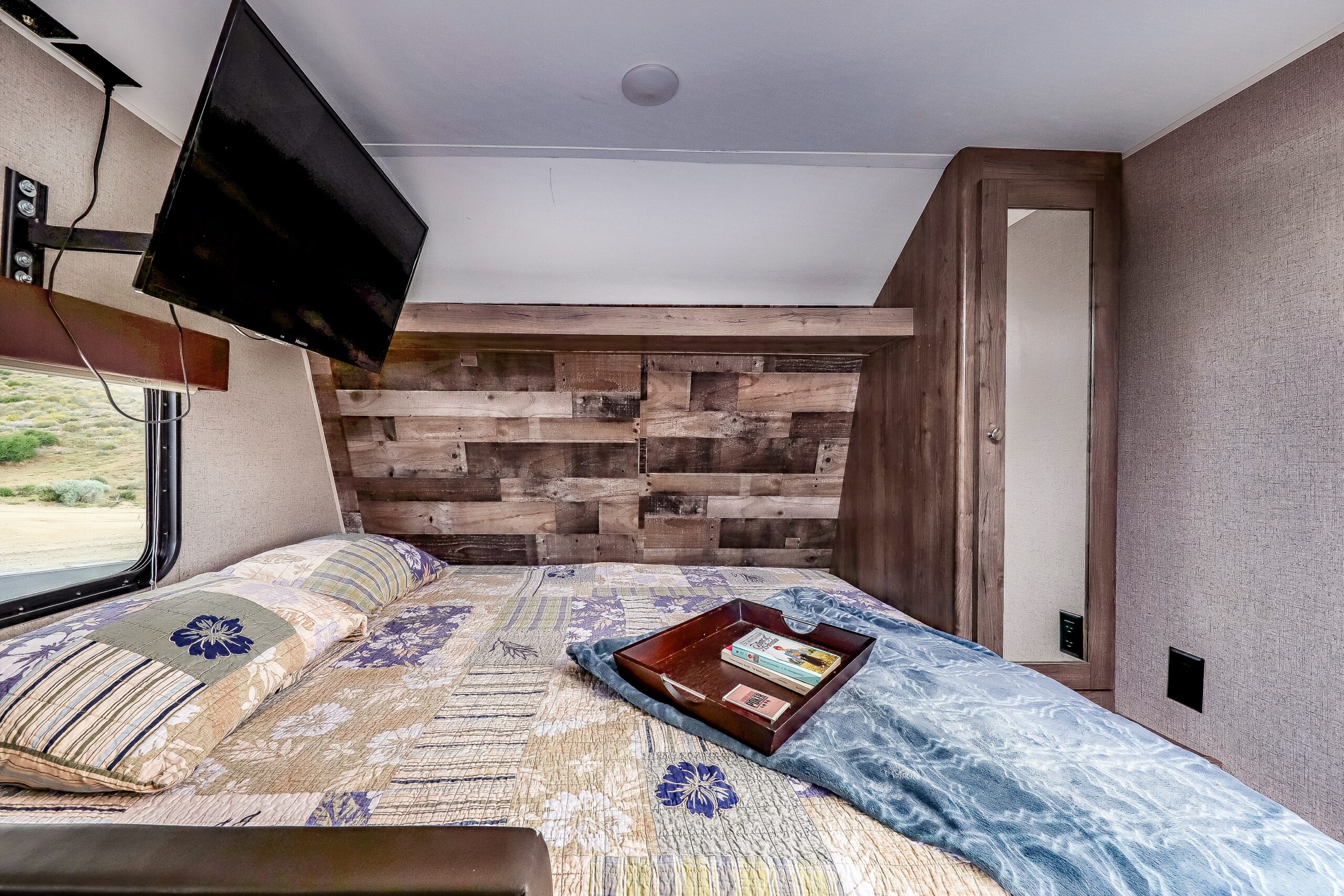 RV rental: inviting bedroom with a cozy patchwork quilt, mounted TV, rustic wood headboard, and scenic window view.. Aspen Trail LE 2020