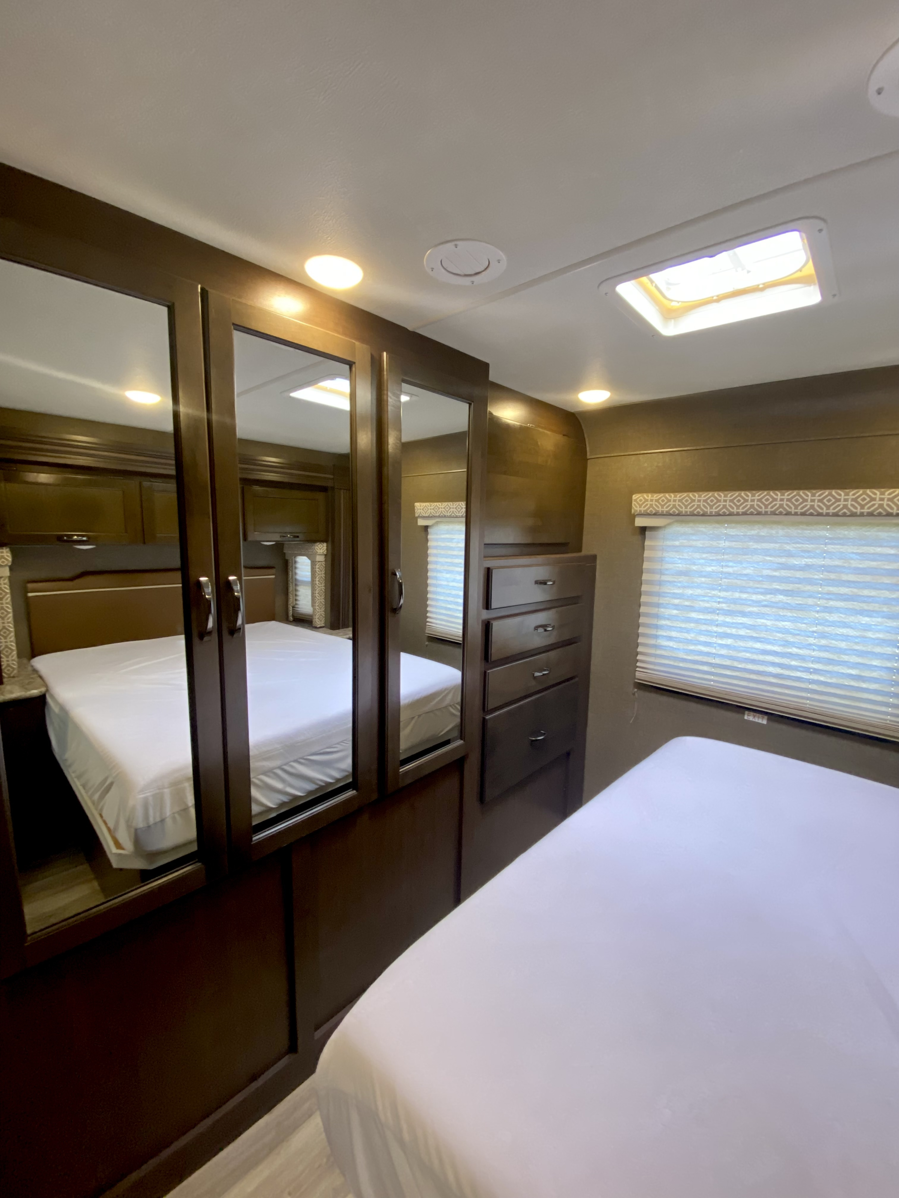 Inside an RV rental: a compact bedroom featuring two beds (one reflected), mirrored closet doors, and built-in drawer storage.. Thor Freedom Elite 2018
