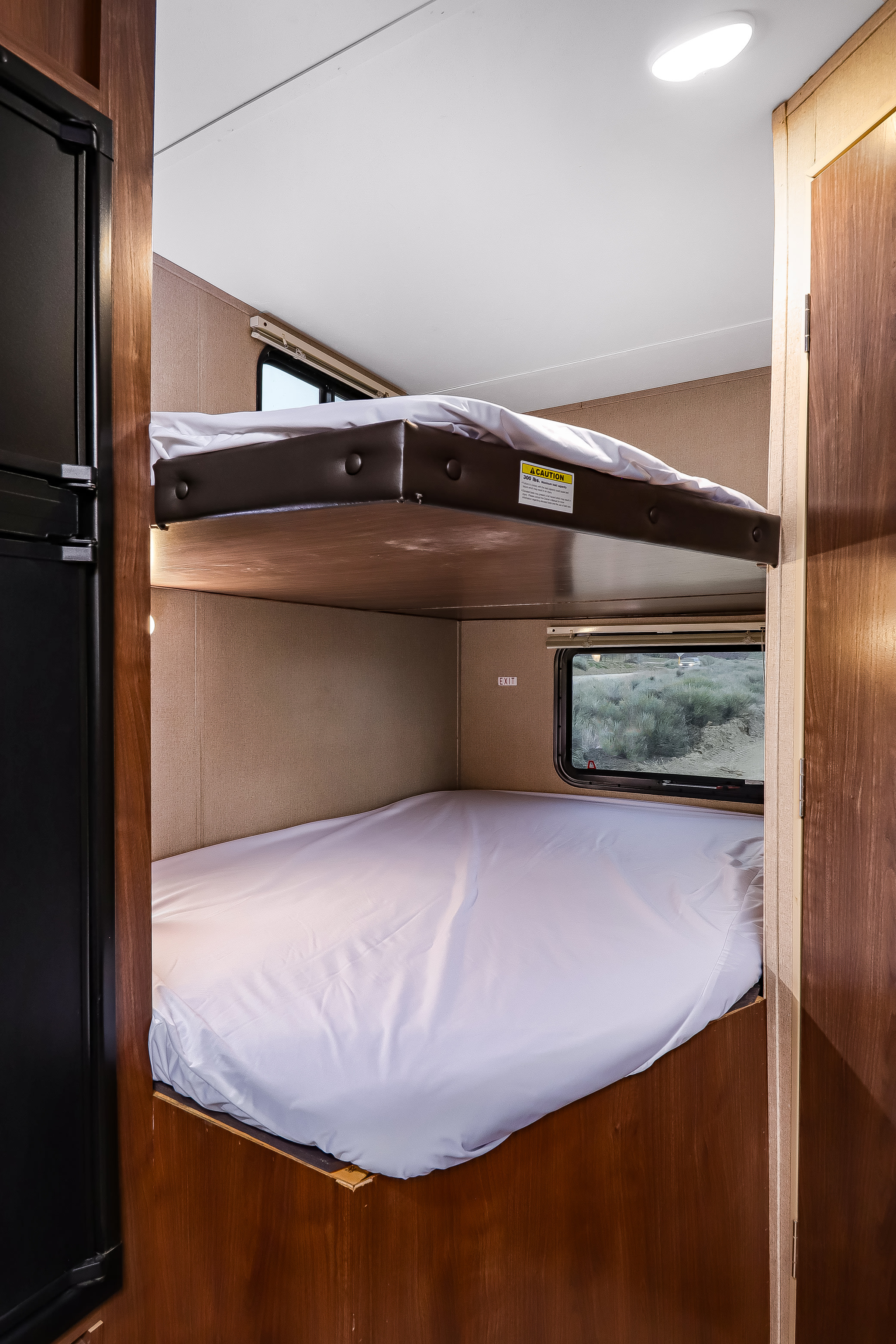 This RV rental interior shows cozy bunk beds with white sheets, a refrigerator, and a window overlooking a natural landscape.. Dutchmen Coleman Lantern 2017
