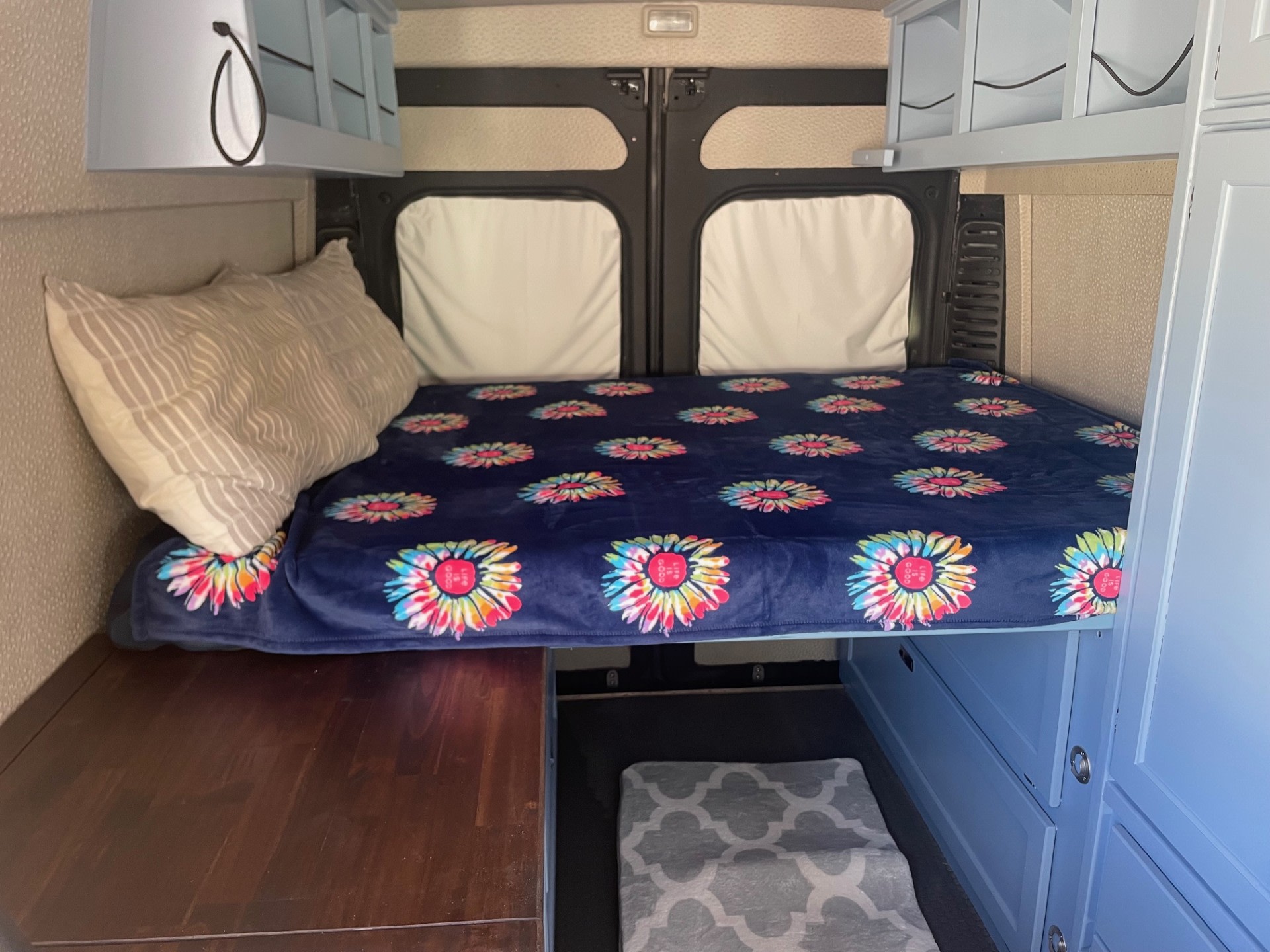Inside a custom RV rental: cozy bed with floral blanket, overhead storage, and under-bed drawers. Perfect for adventure!. Dodge Promaster Highroof 2019