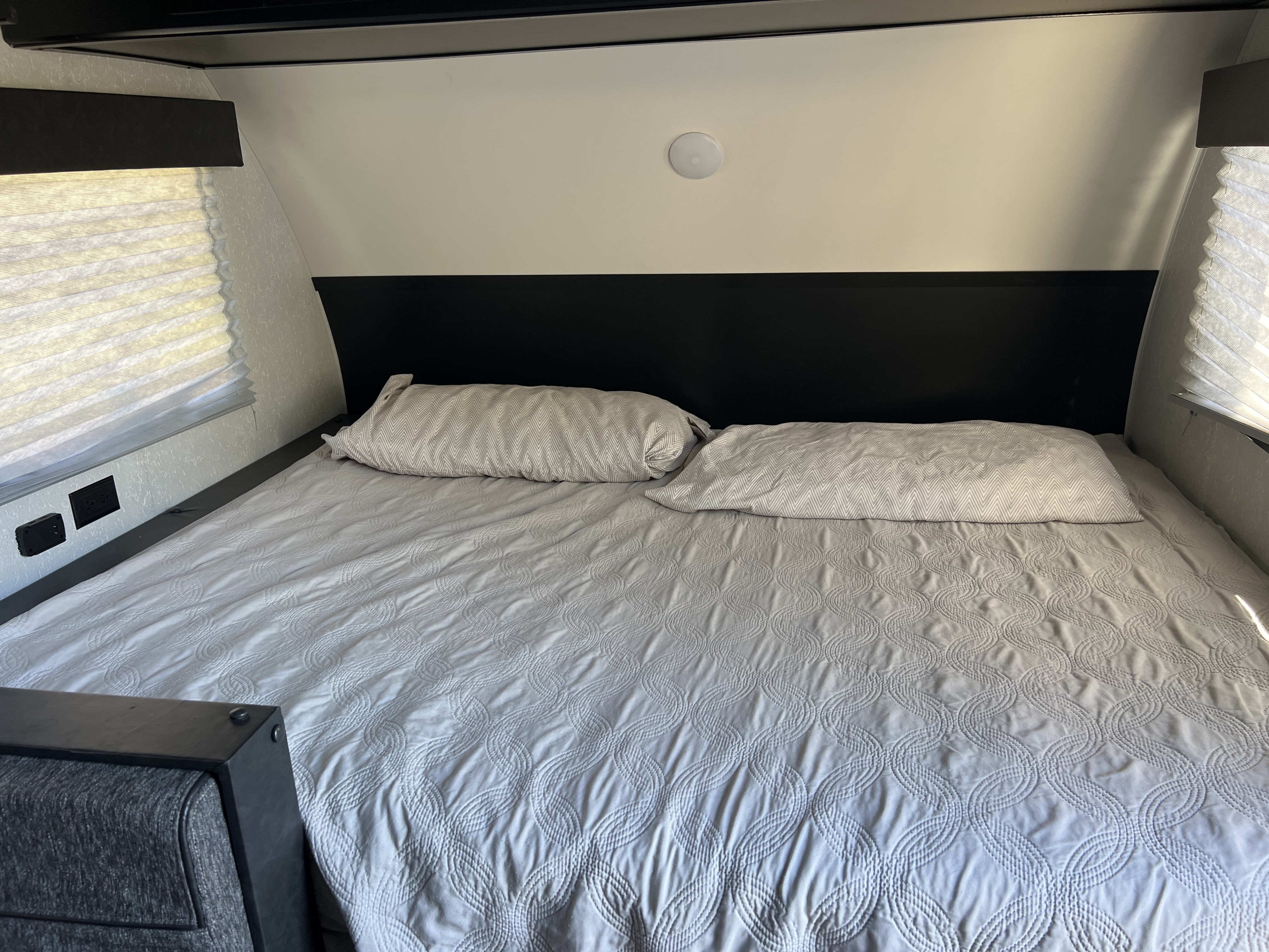 RV rental bedroom interior featuring a large bed with light quilted bedding, pillows, and privacy blinds.. Forest River Cherokee Wolf Pup 2022