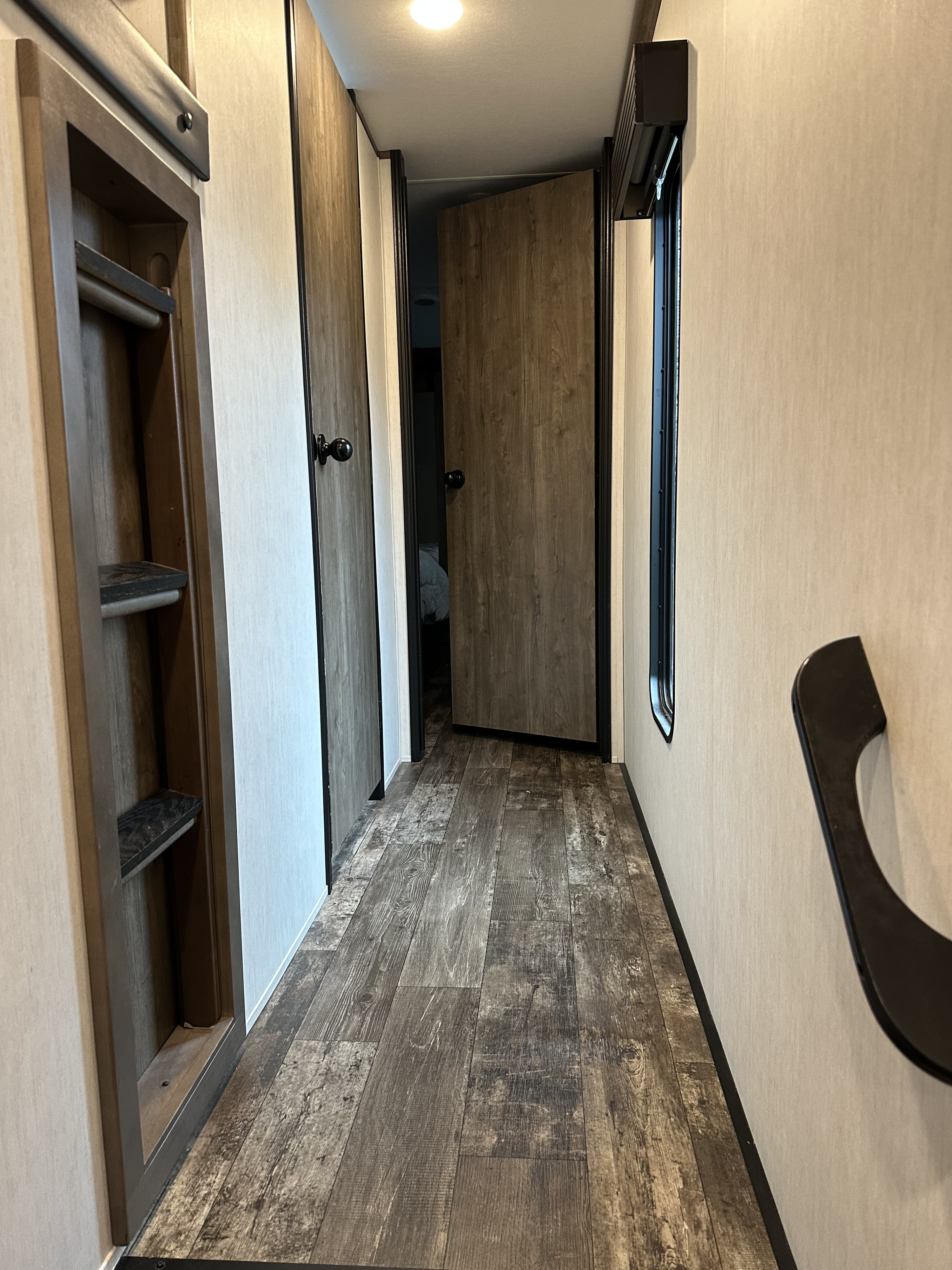 RV rental interior: A narrow hallway with wood-look flooring, built-in storage, multiple doors, and a window, typical for RV travel.. Forest River Sabre 2022