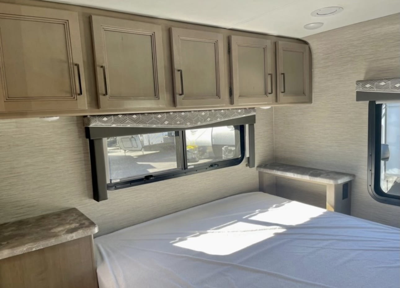 RV rental bedroom: overhead storage cabinets, a bed, and windows providing natural light.. Thor Four Winds 2023