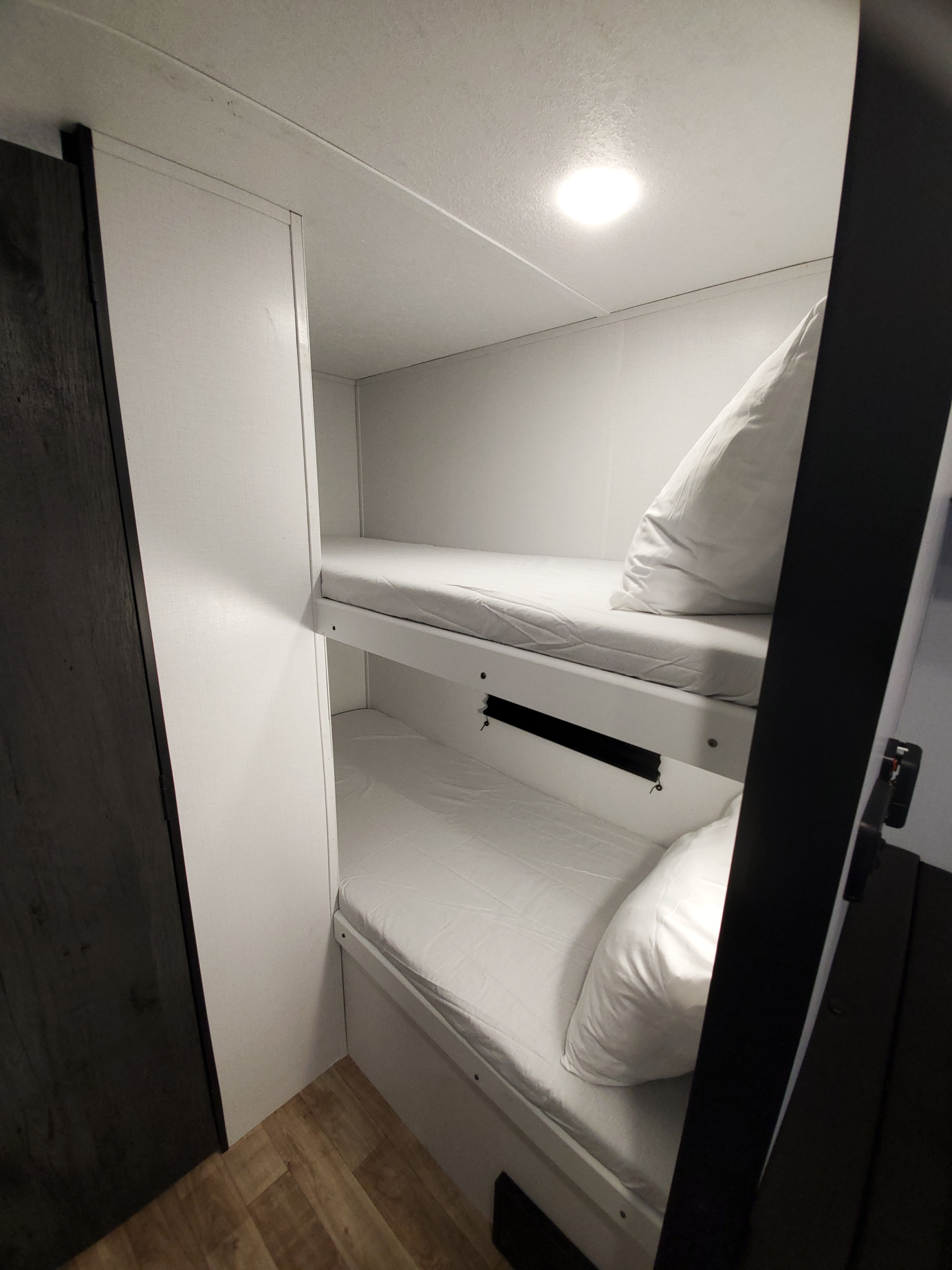 Bright white bunk beds in an RV rental, ready for travelers. Features soft pillows, clean sheets, and a ceiling light.. Keystone RV Hideout 2021