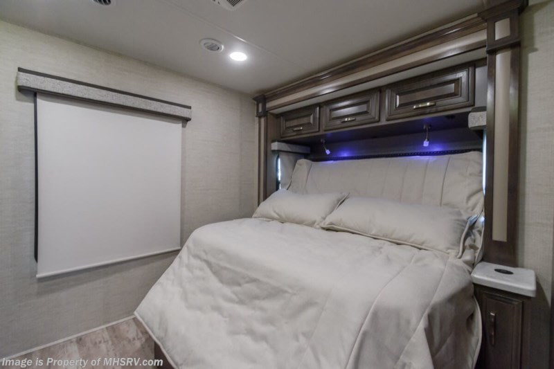 Cozy RV rental bedroom features a plush bed, stylish overhead cabinets, blue accent lighting, and a window blind.. Entegra Coach Accolade 2023