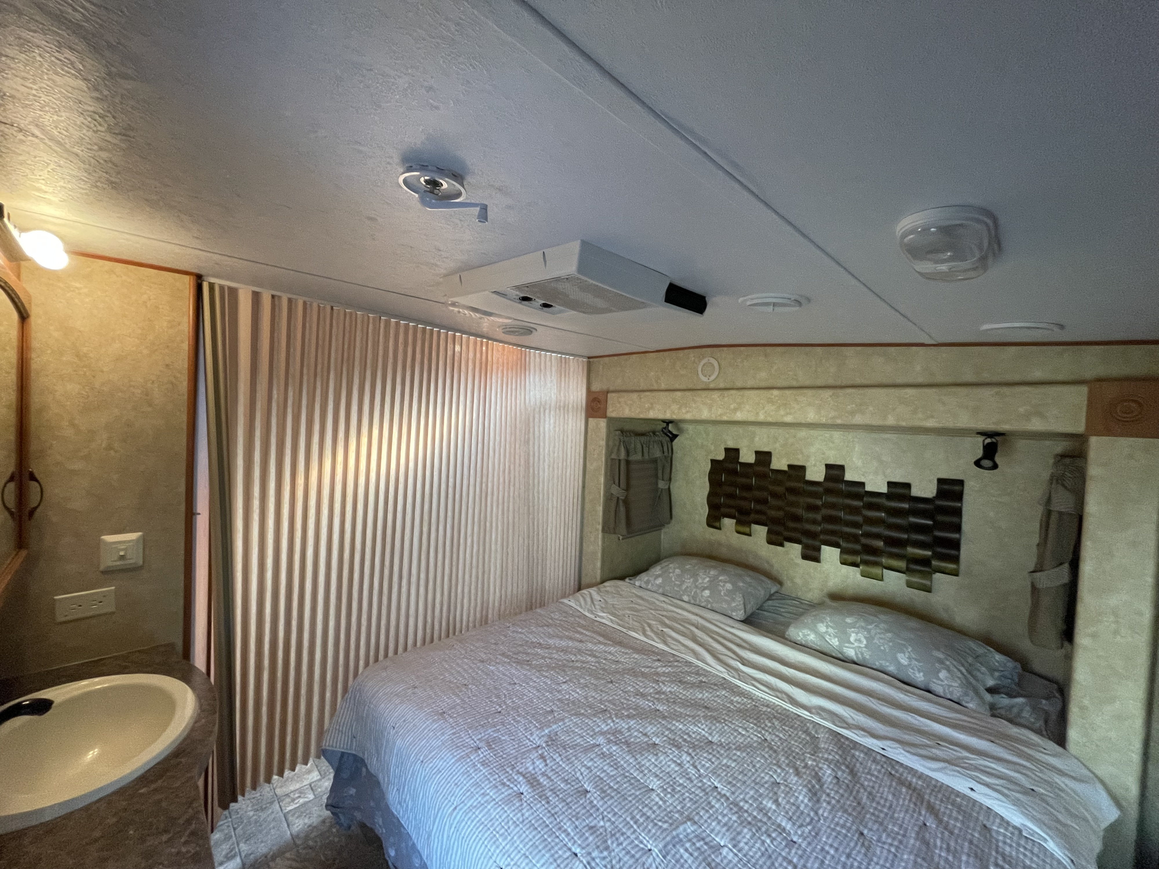 An RV rental bedroom features a cozy bed, adjacent sink, and textured ceiling with AC, offering practical comfort.. Forest River Sierra 2012