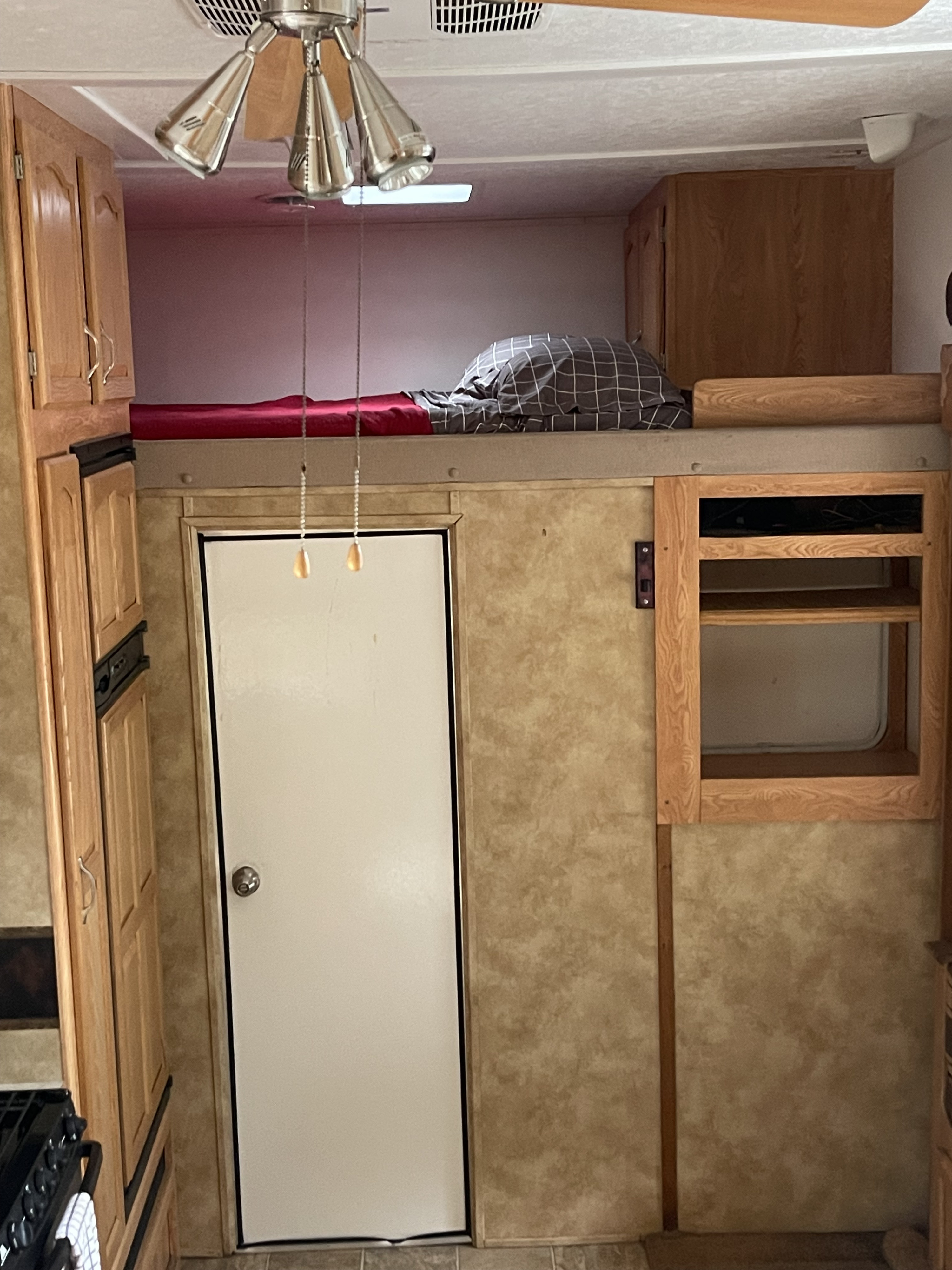 RV rental's bunk bed with red & plaid bedding, door, wood cabinets, ceiling fan, & kitchen area view.. Keystone RV Raptor Toy Hauler 2006