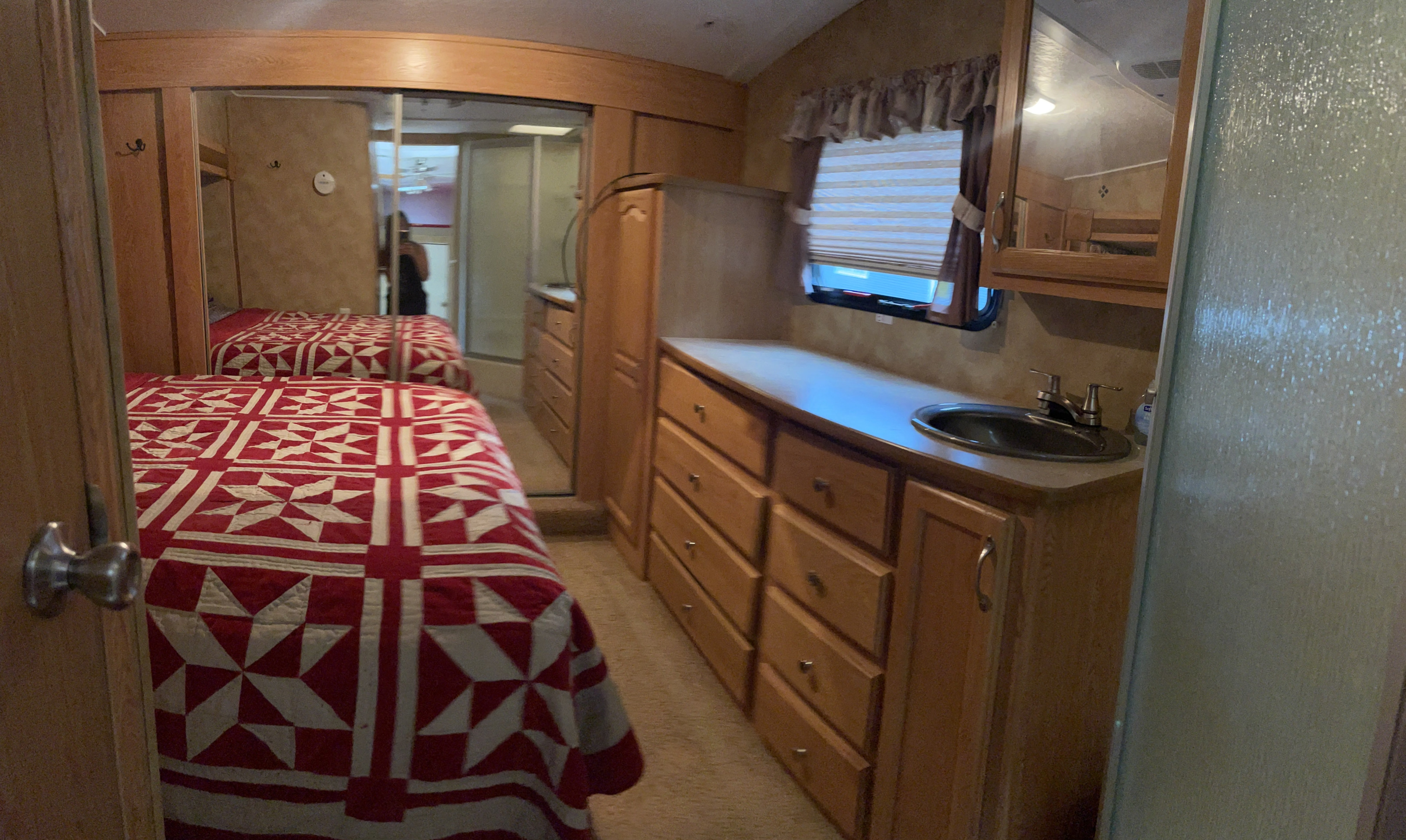 RV rental interior: bedroom with red quilt, wood vanity, sink, mirrored cabinet, and shower. Comfort for your travels.. Keystone RV Raptor Toy Hauler 2006
