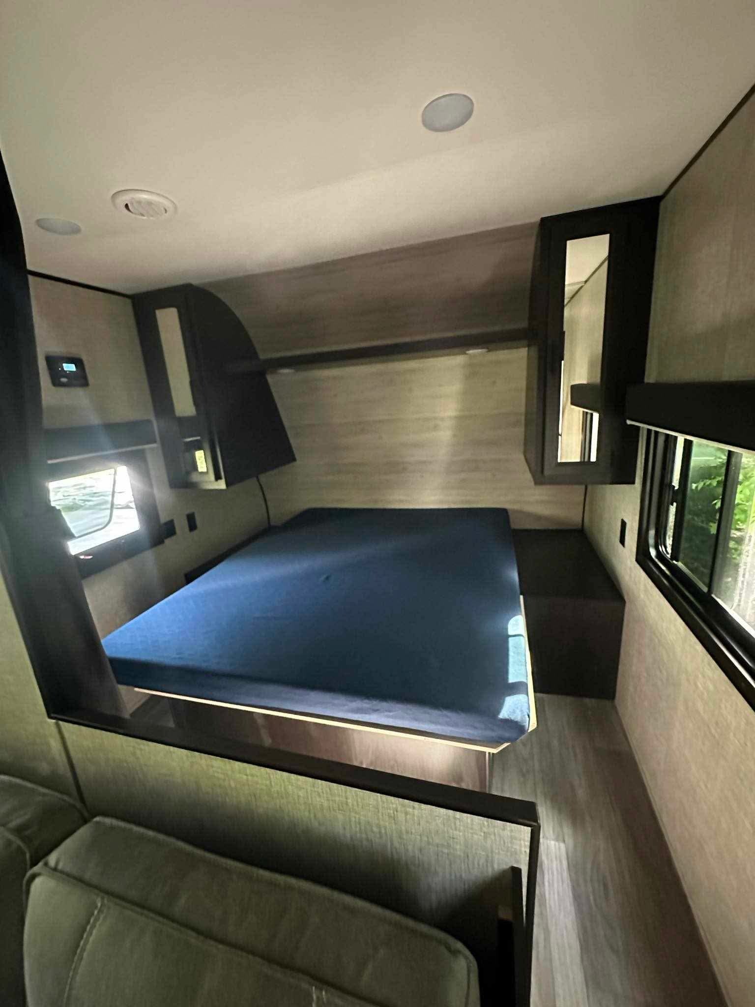 Compact RV rental bedroom, featuring a blue mattress, adjacent seating, and bright windows.. Jayco Jay Flight SLX 2022