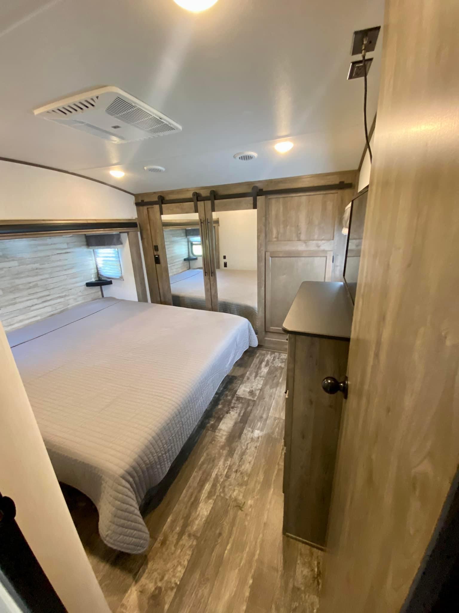 RV rental bedroom interior: large bed with gray cover, mirrored closet, wood floor, AC, and dresser for cozy travels.. Forest River Sabre 2021