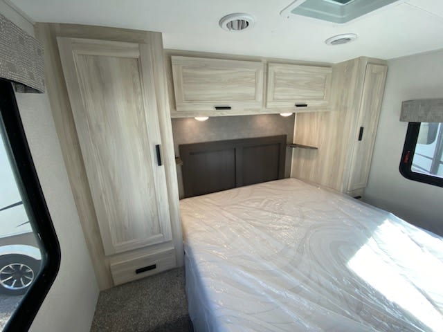 This RV rental's bright bedroom features a bed, overhead cabinets, and two wardrobes, ready for your next adventure.. Forest River Sunseeker LE 2022