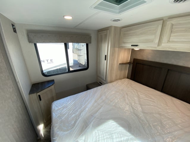 Interior of an RV rental bedroom showing a bed, storage cabinets, and a window. Perfect for your travels.. Forest River Sunseeker LE 2022