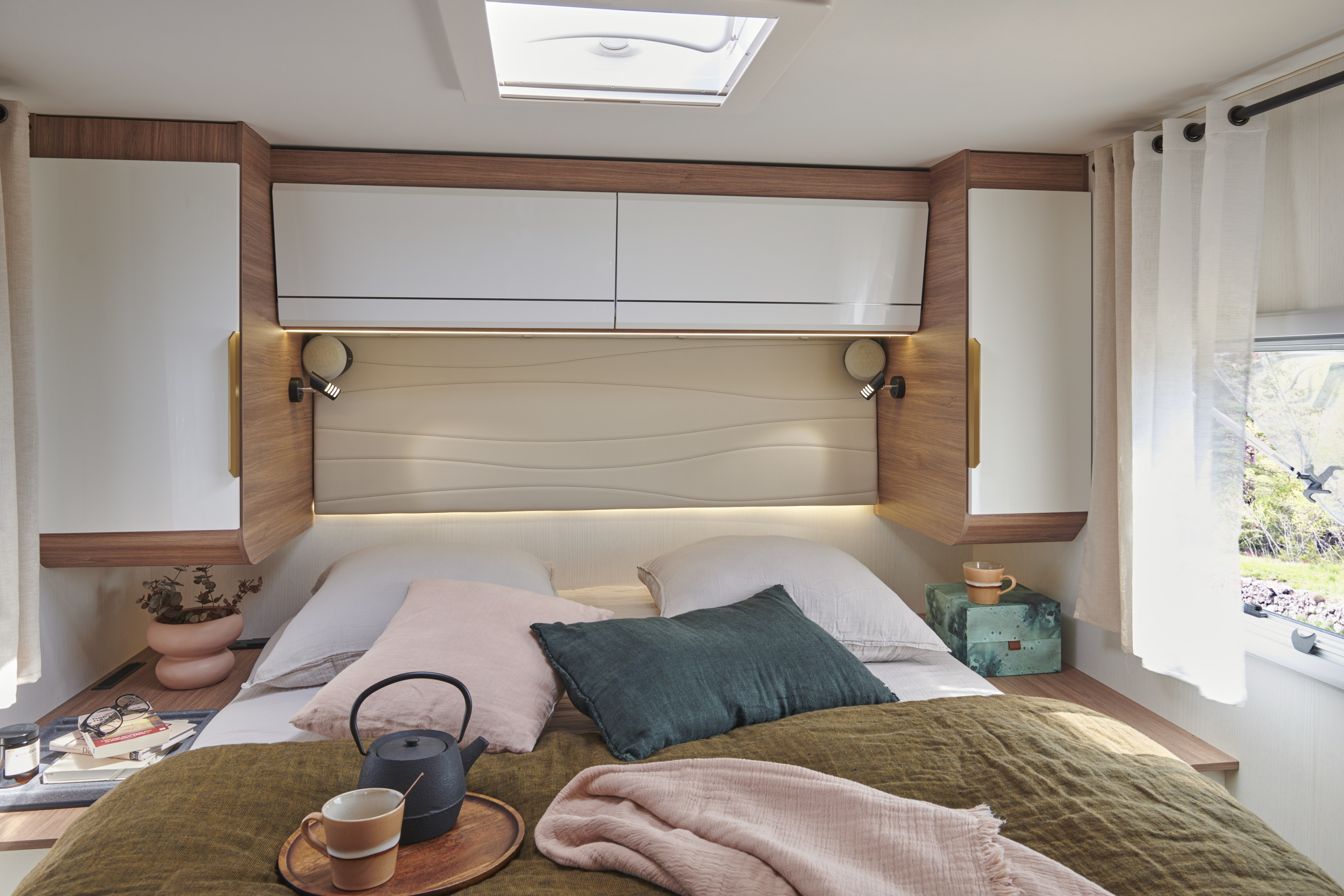 A cozy RV rental bedroom interior features a comfy bed with soft blankets, bedside storage, accent lighting, and a view of nature.. Pilote G740FC EVIDENCE 2025